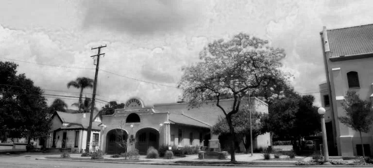 A black and white photo of a the Glendora Historical Museum housed in the city's original city hall, surrounded by trees and vintage buildings.