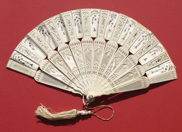 Decorative hand fan with intricate cutout designs, and a tassel hanging from the handle, on a red background.