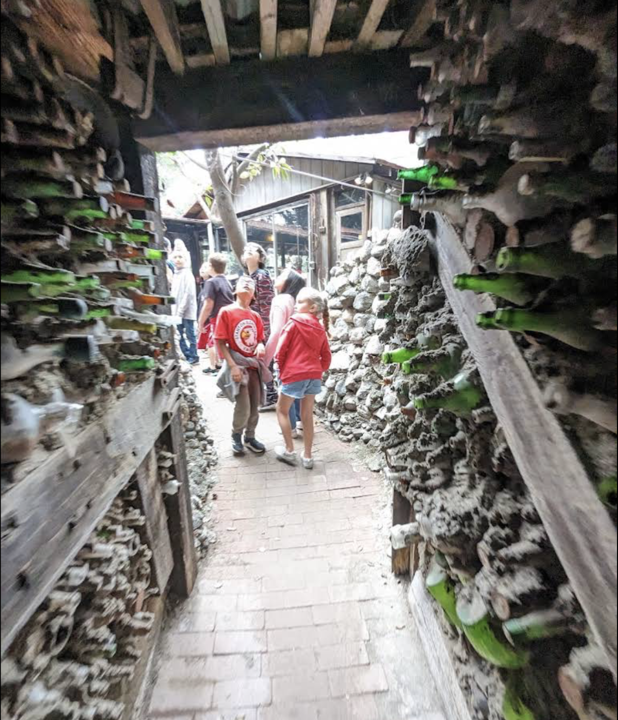 People walking through a tunnel at Rubel Castle. The tunnel is lined with glass bottles.