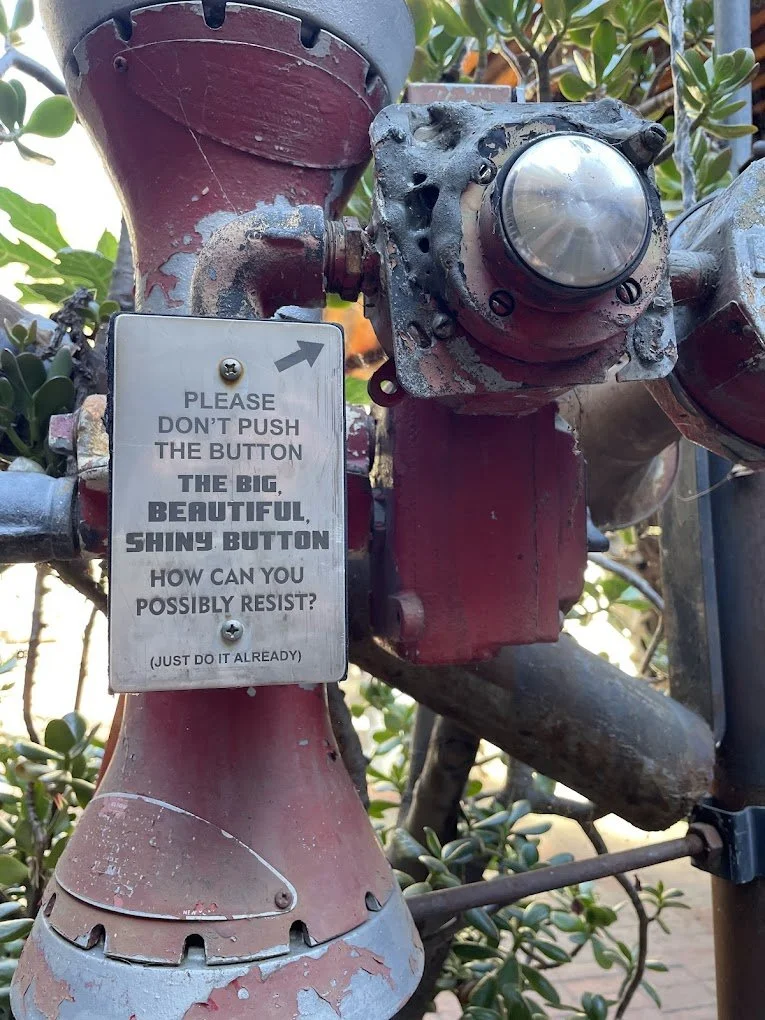 Metal button mounted in a pipe structure at Rubel Castle, with a sign reading “Please don’t push the button.”