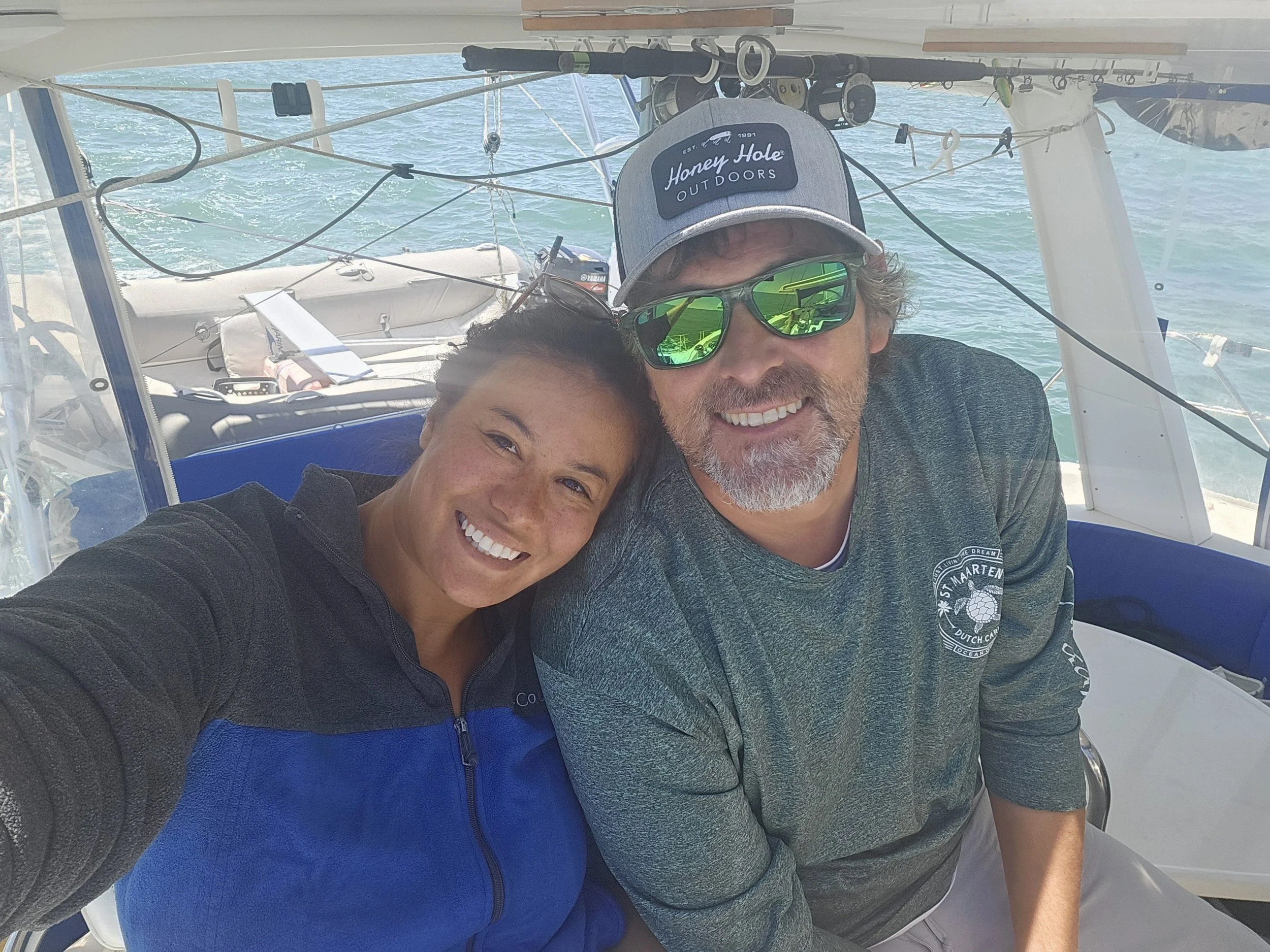 Two people smiling on a boat, with water visible in the background.