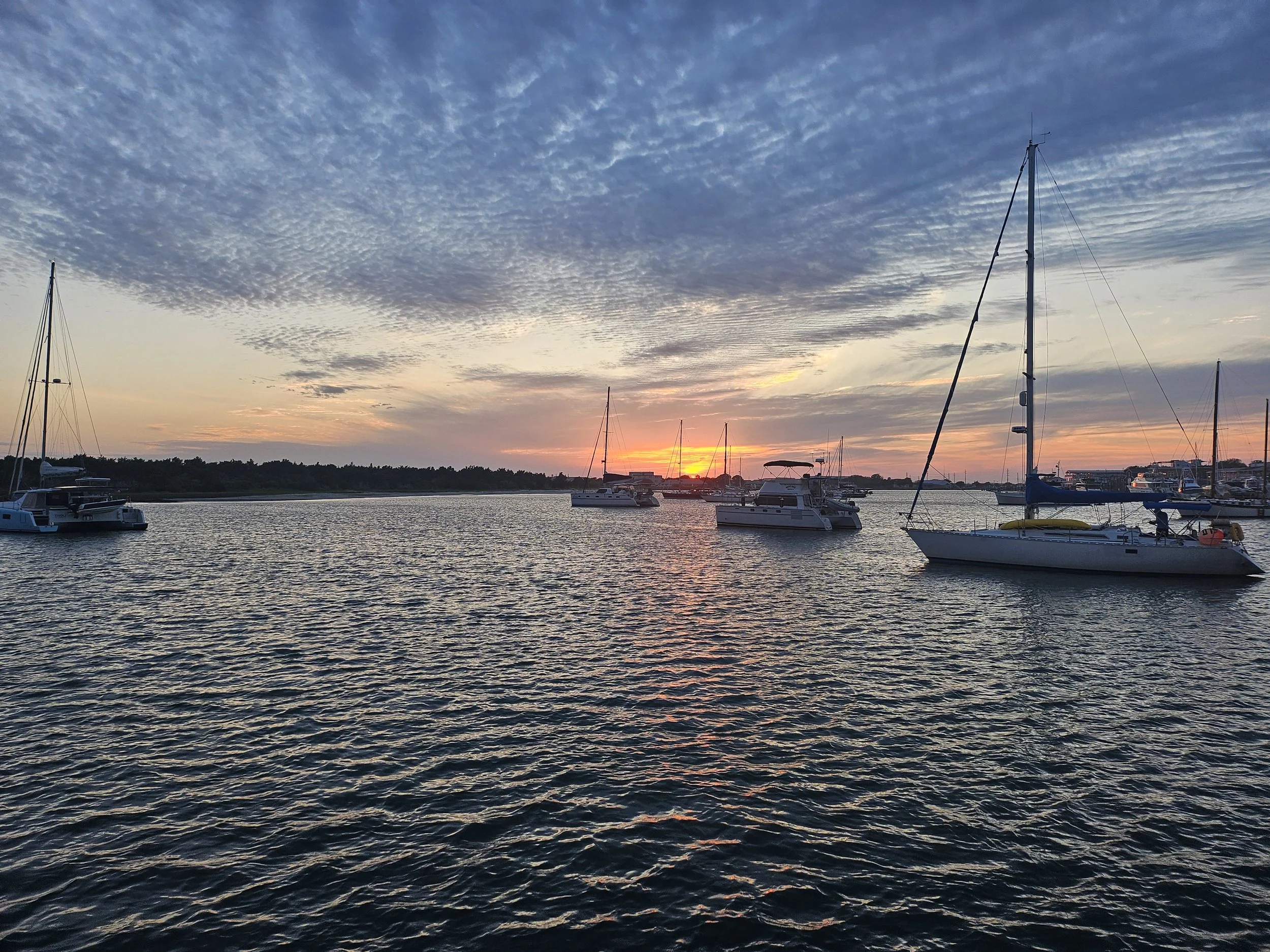 Sailboats anchored on a body of water at sunset with a colorful sky and clouds.
