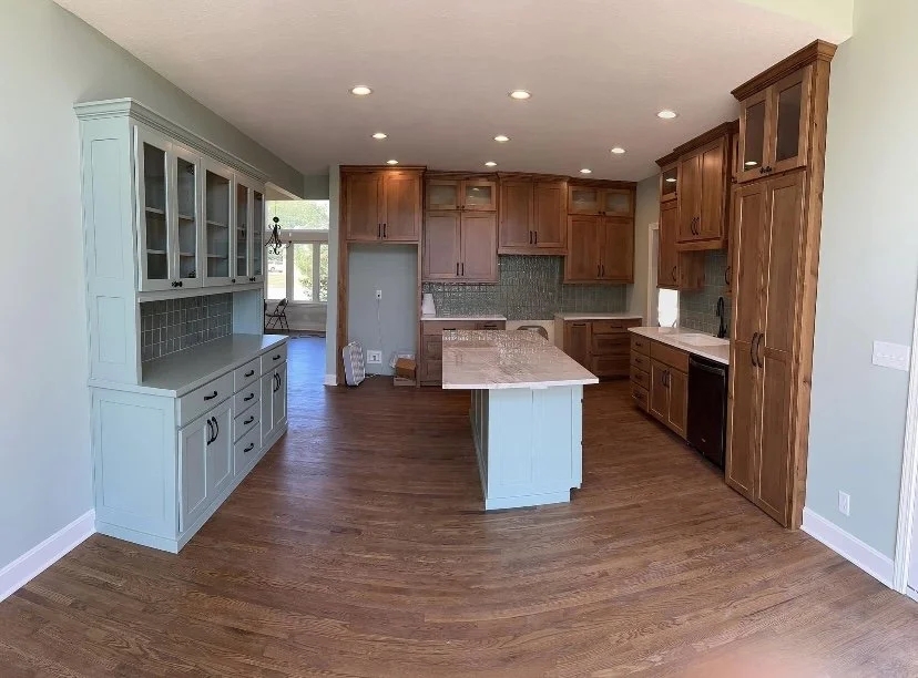 Open kitchen with light green and natural wood cabinets, a kitchen island, hardwood floors, and a window with a view outside.