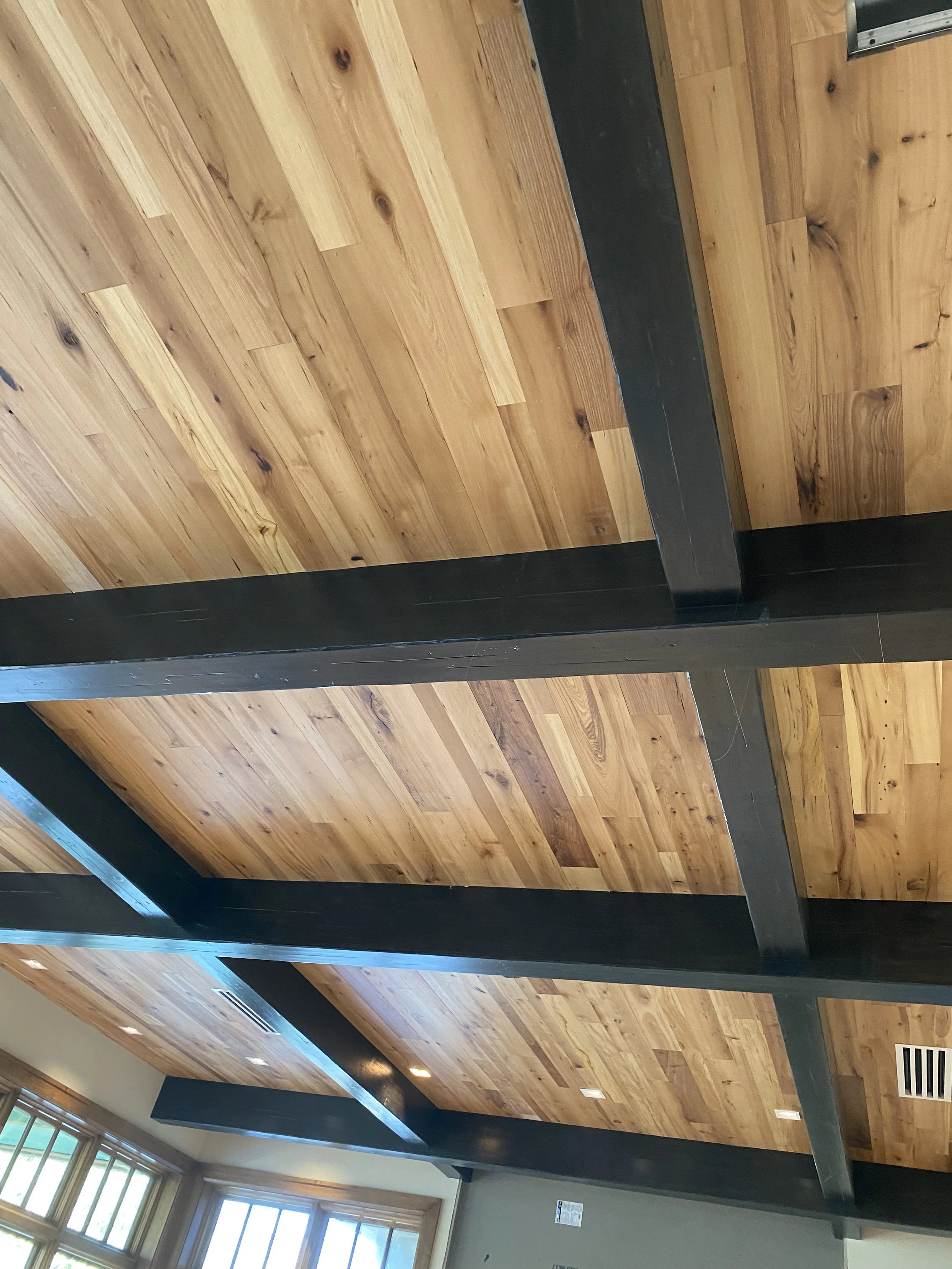 Ceiling with wooden panels and black structural beams, and windows with natural light.