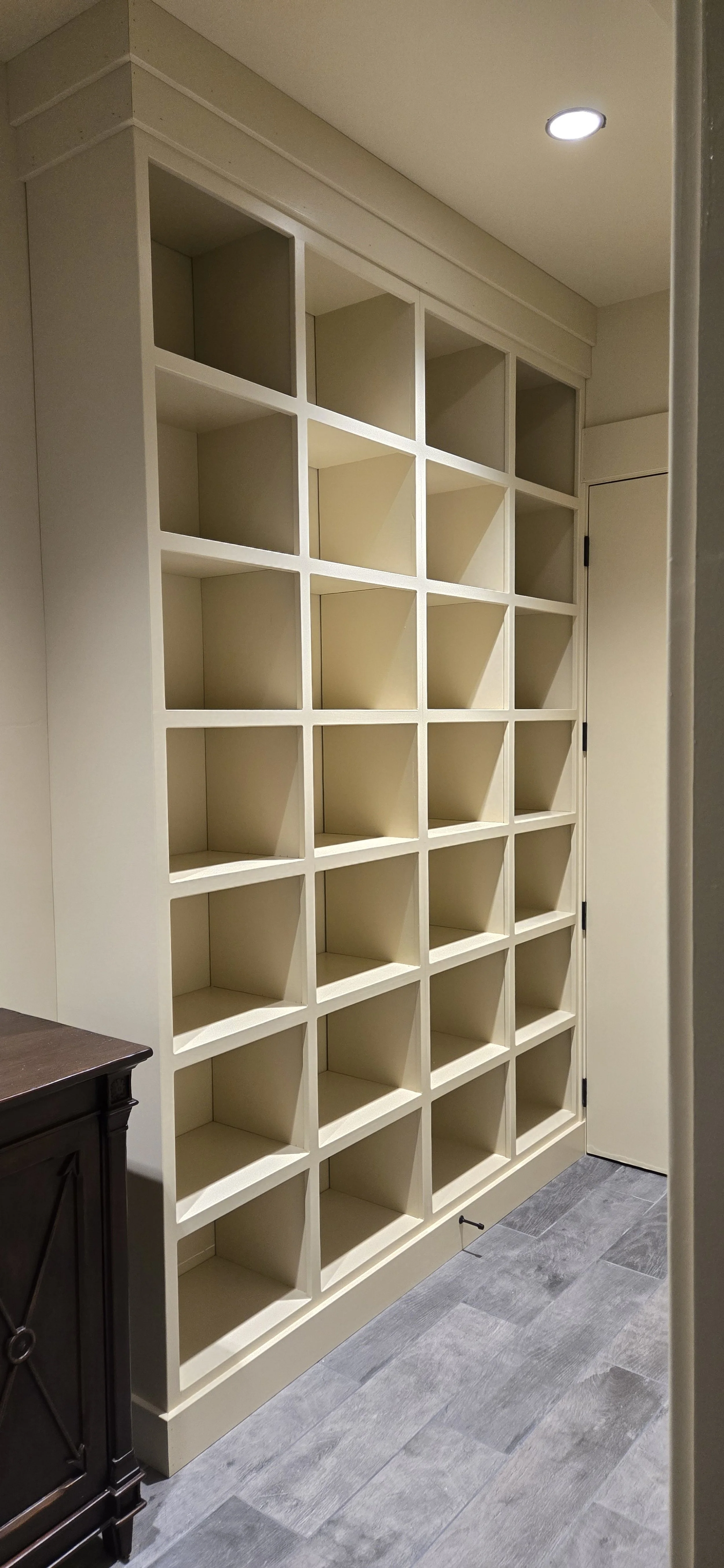 Empty cream-colored built-in bookshelf with many square compartments next to a door, on a gray wood floor.