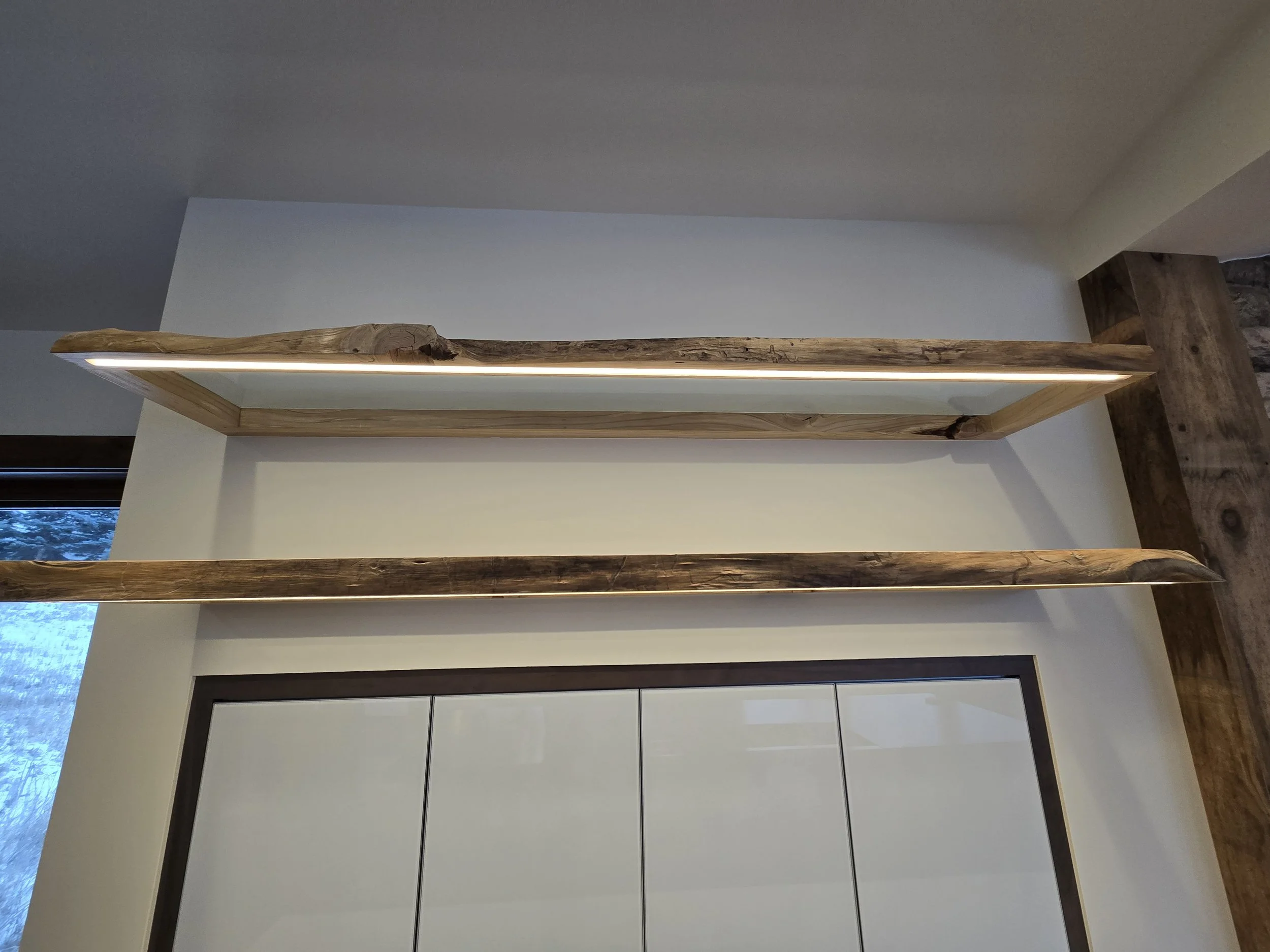 Two wooden floating shelves with natural edges mounted on a white wall above white cabinet doors.
