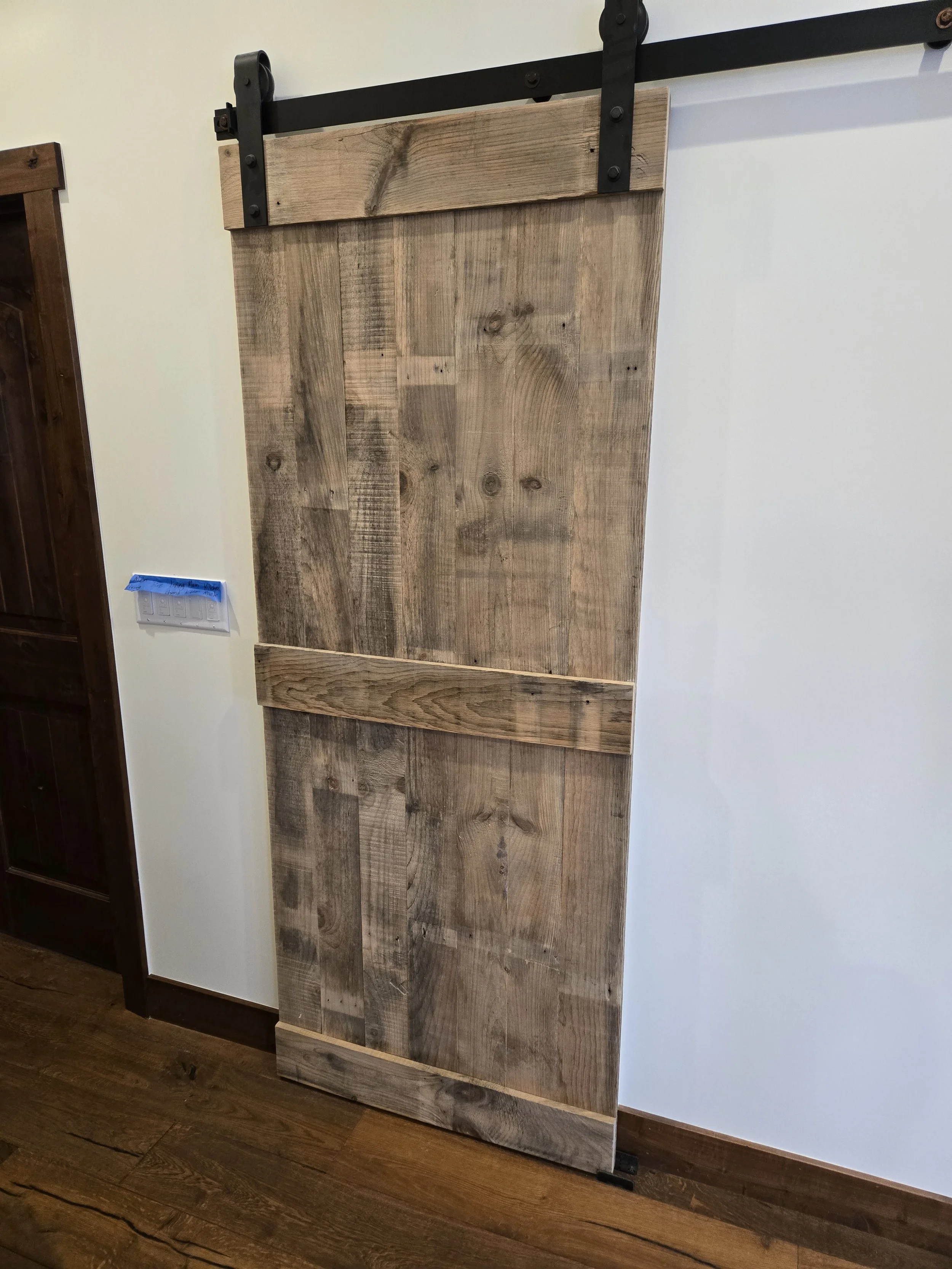 A rustic wooden sliding barn door with black metal hardware hanging on a white wall.