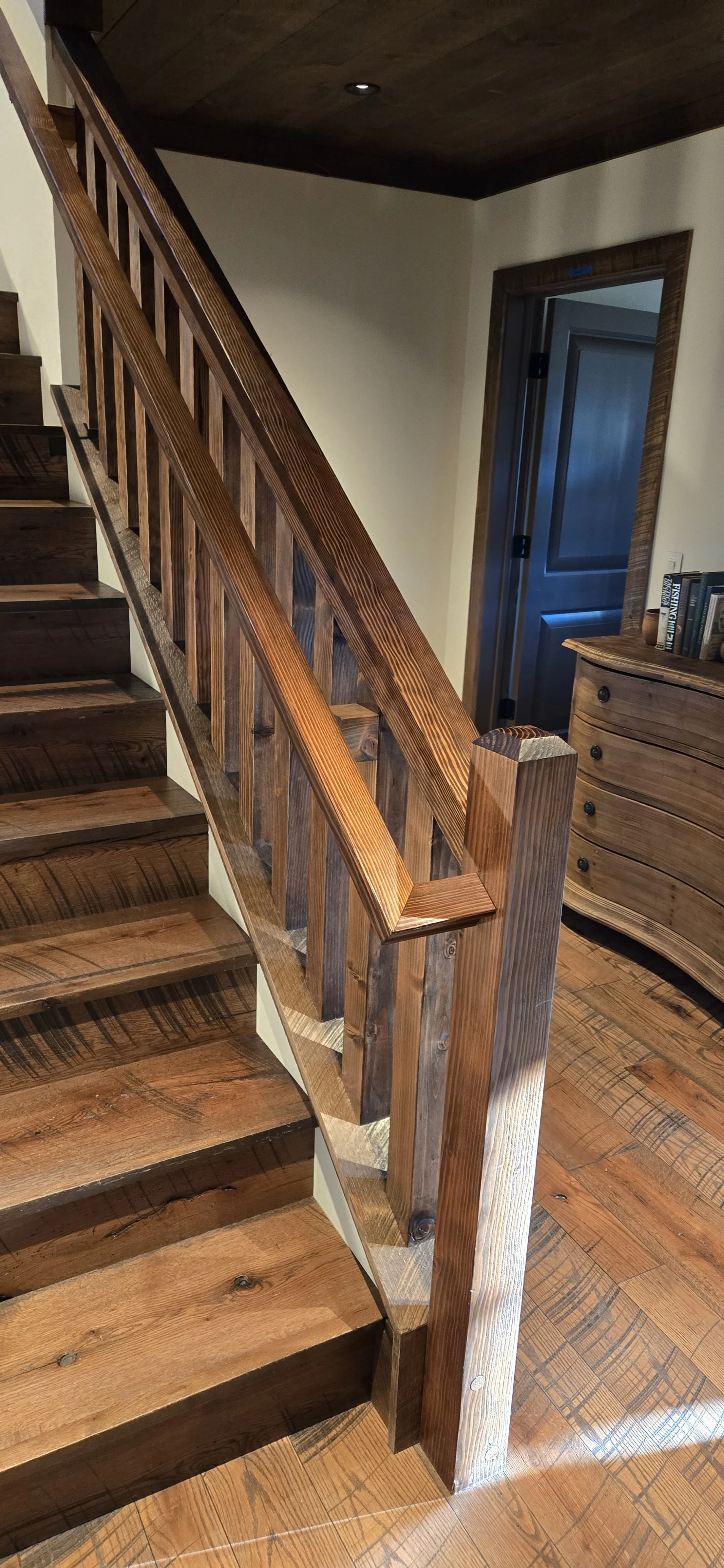 Wooden staircase and railing inside a house, with a wooden dresser and books in the background.