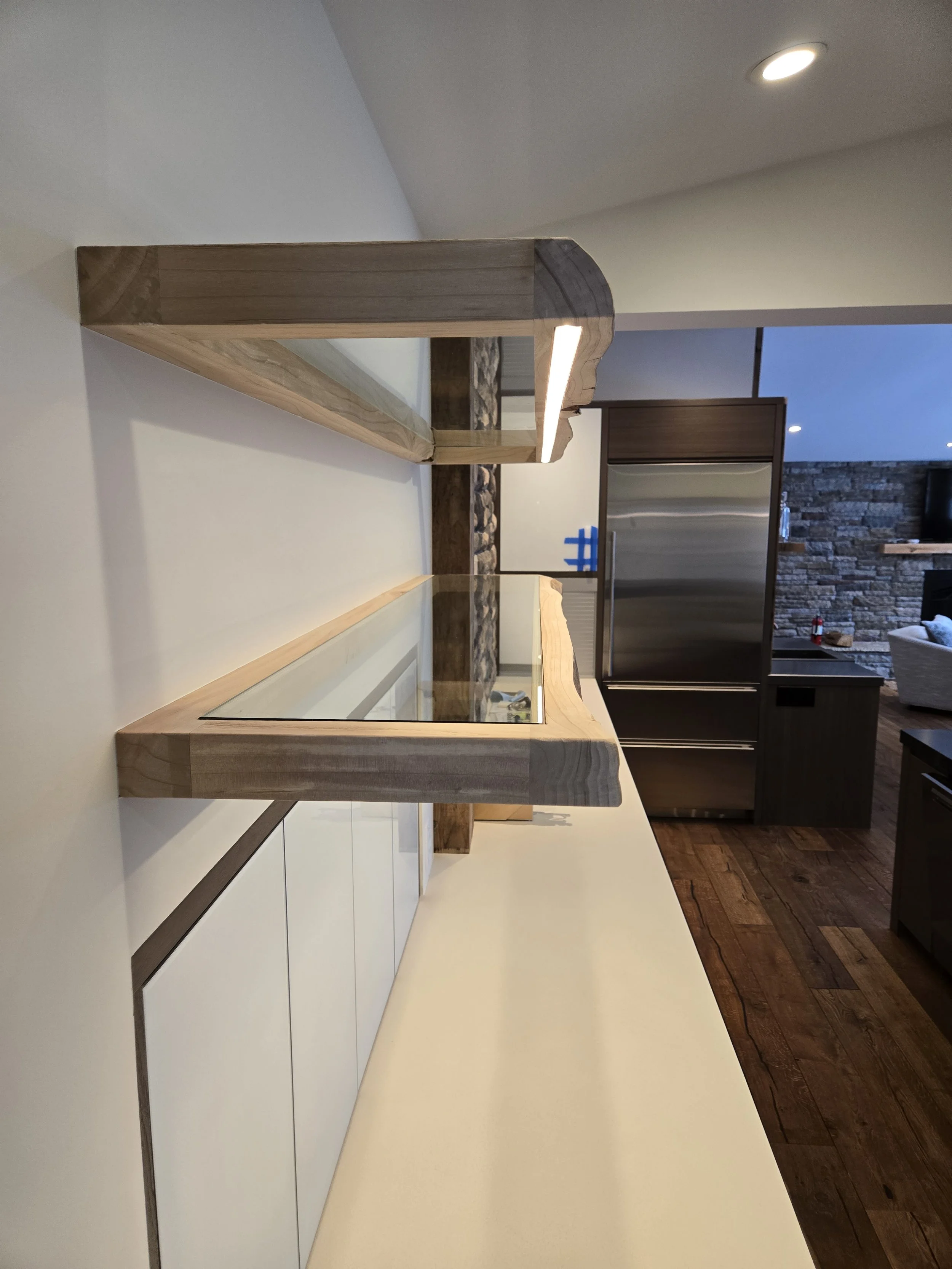 Wooden and glass display case on a white countertop in a modern kitchen with wooden flooring, stainless steel appliances, and a stone accent wall.