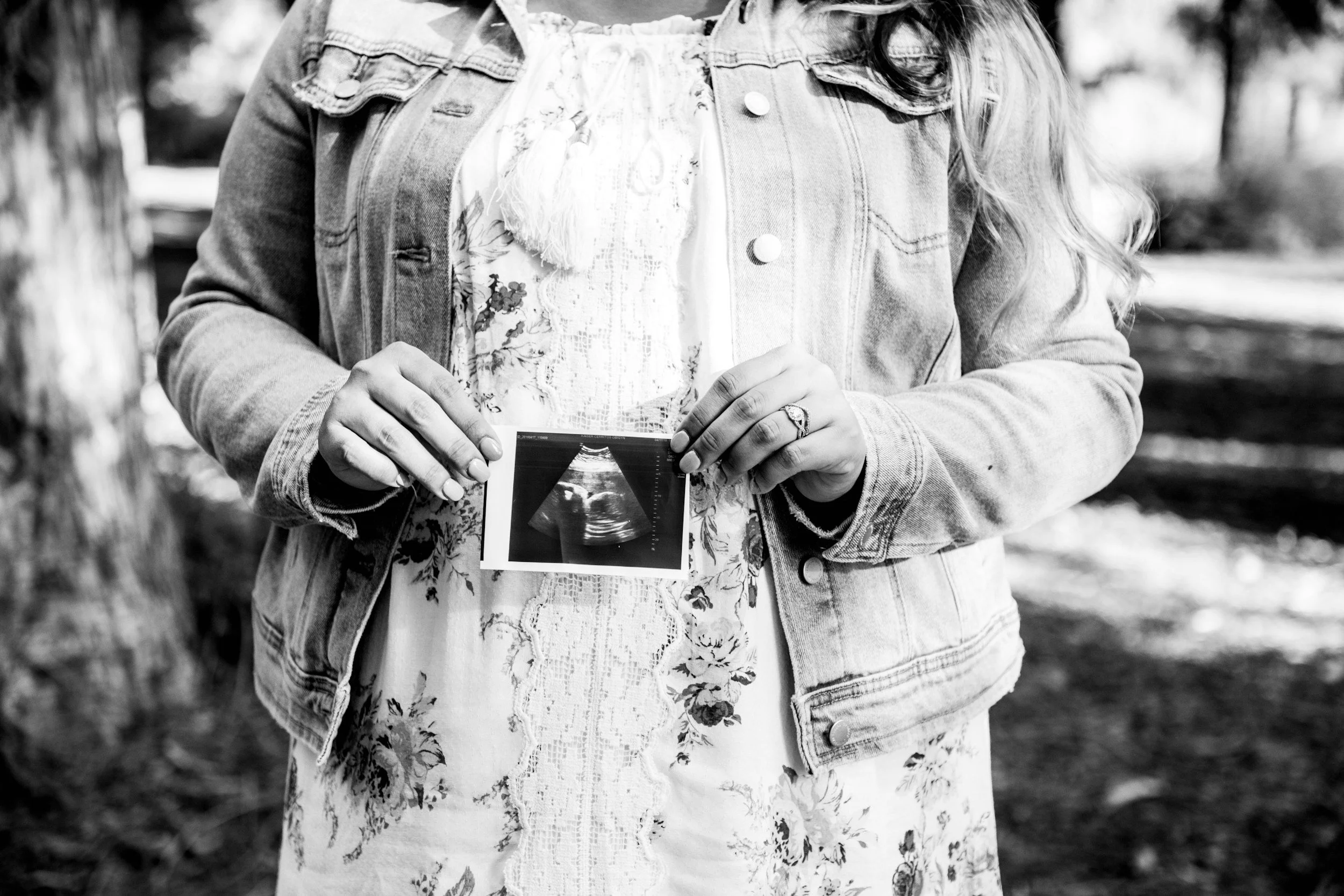 A woman in a floral dress and denim jacket holding an ultrasound image.