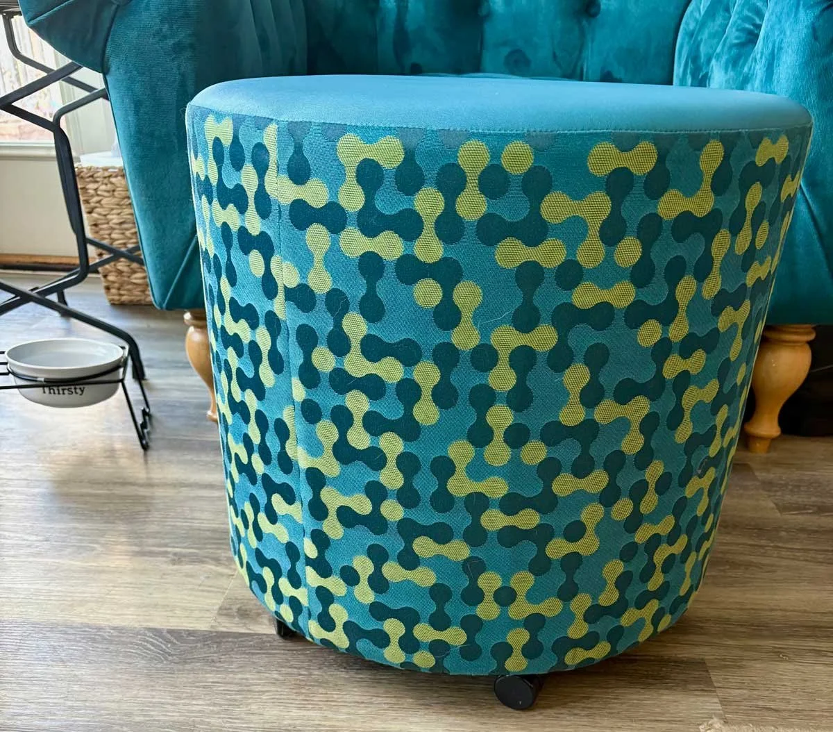 Colorful patterned ottoman with green and dark blue dots on a blue background, in a living room with a blue sofa and a black and white side table.