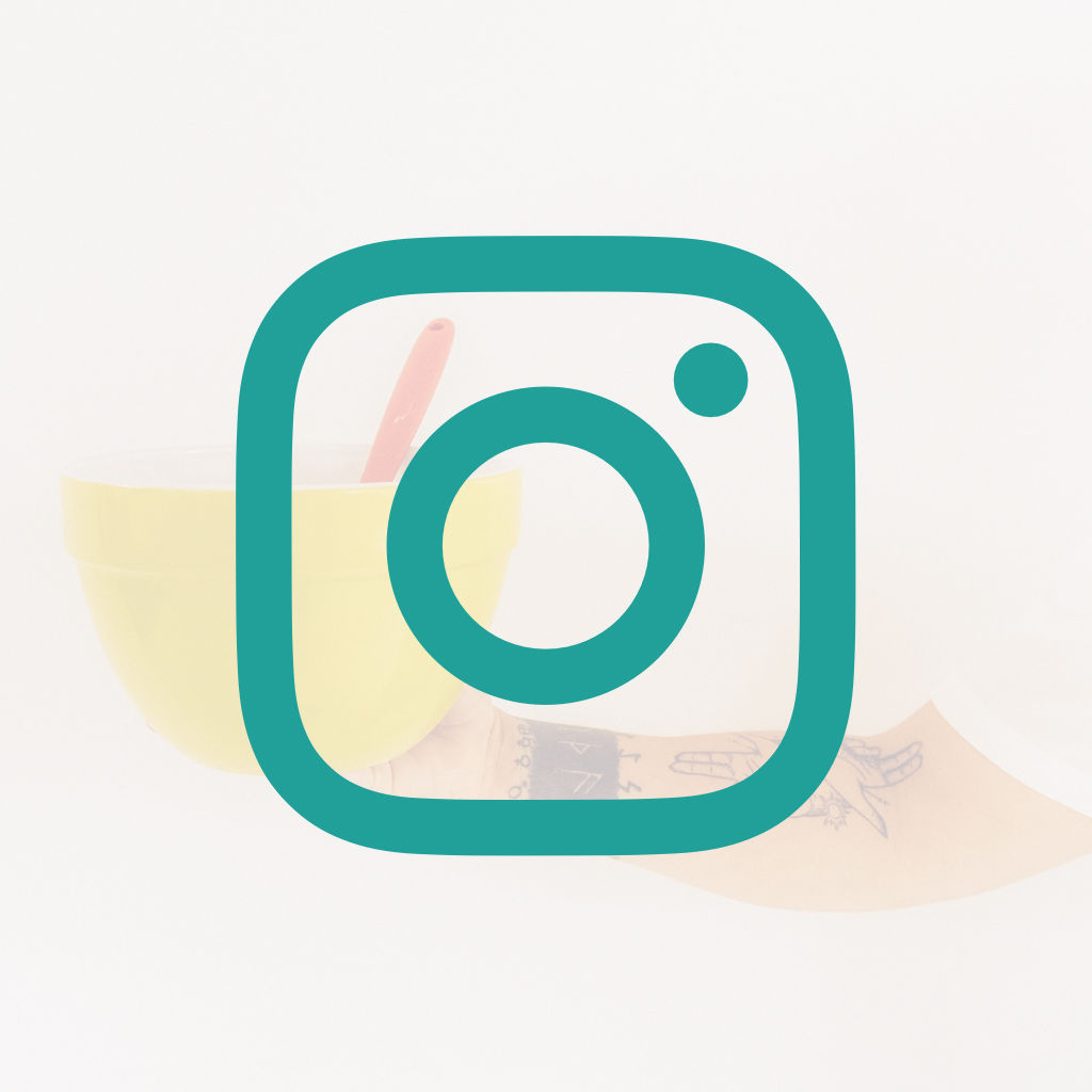 A yellow bowl with a pink spoon and a tattooed arm holding the bowl against a white background.