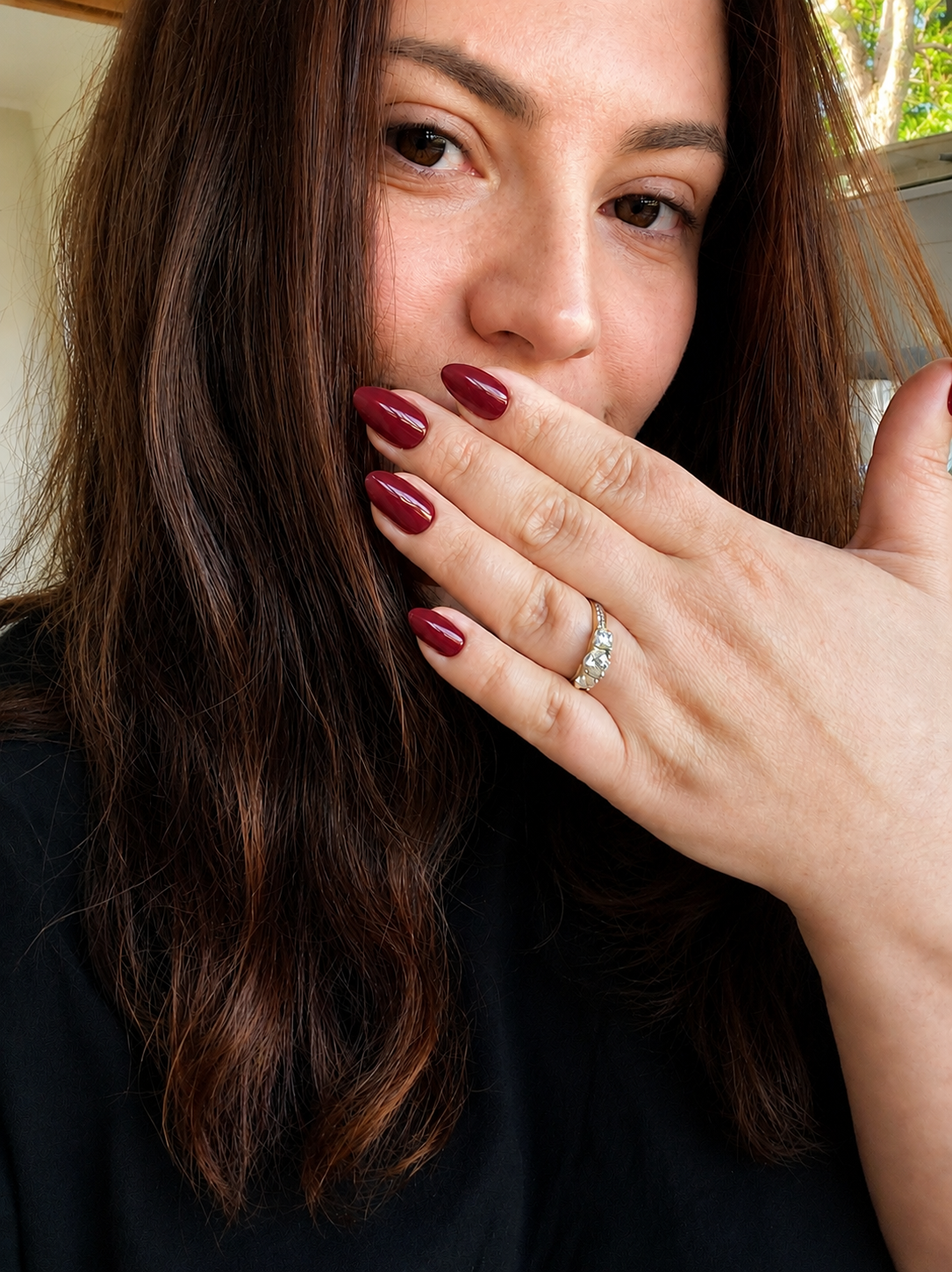 A woman with brown hair and brown eyes showing off her red painted nails and a diamond ring on her left hand.