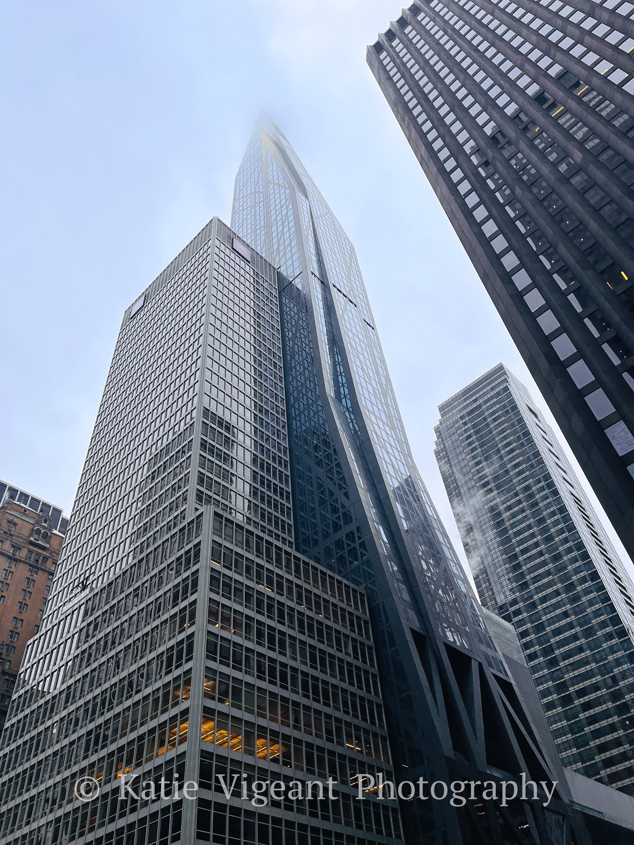 Low-angle view of tall skyscrapers with reflective glass facades in a city featuring high-rise buildings shrouded in fog or clouds.
