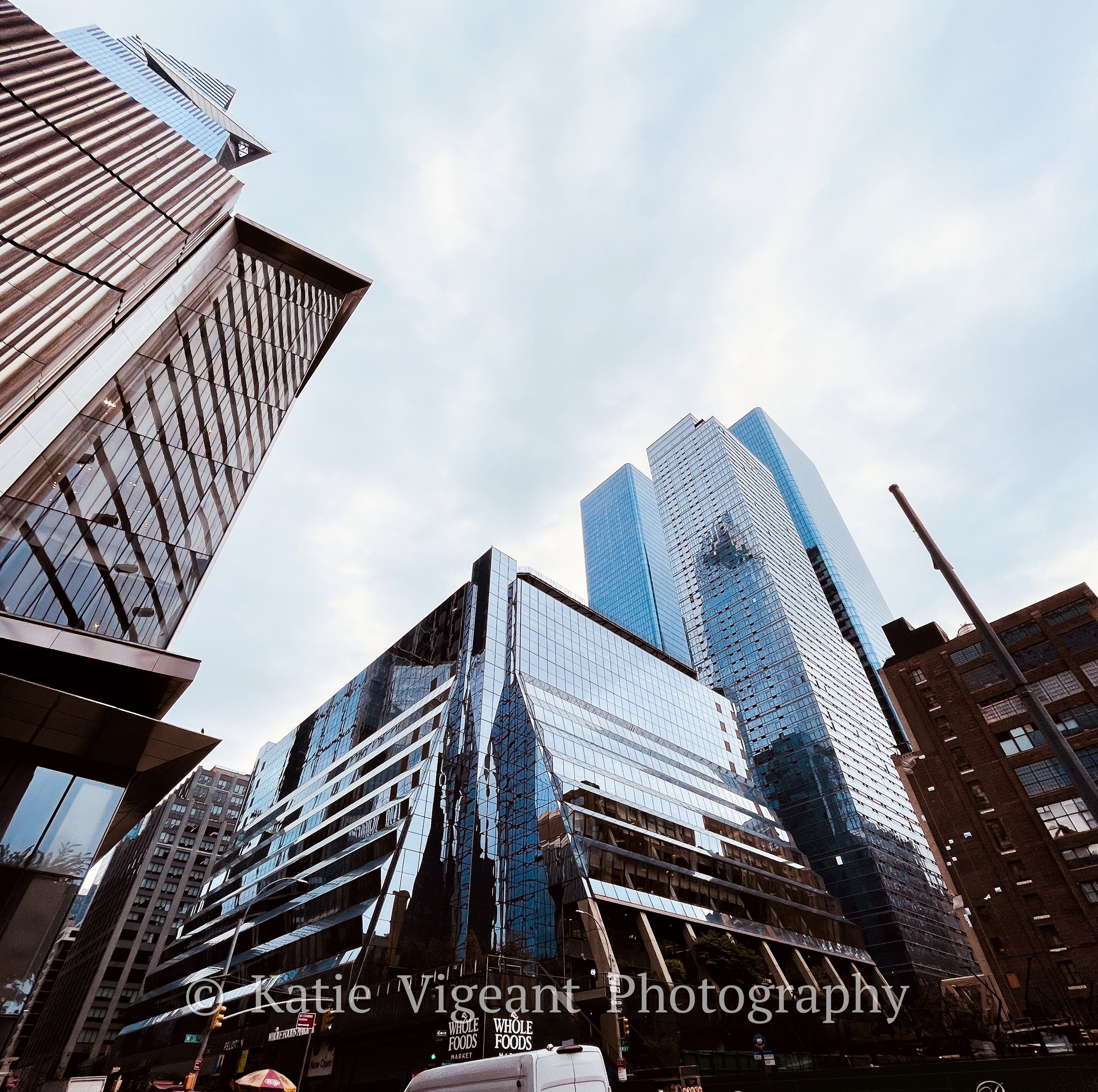Low-angle view of tall modern skyscrapers with glass facades reflecting the sky and surrounding buildings in an urban cityscape.