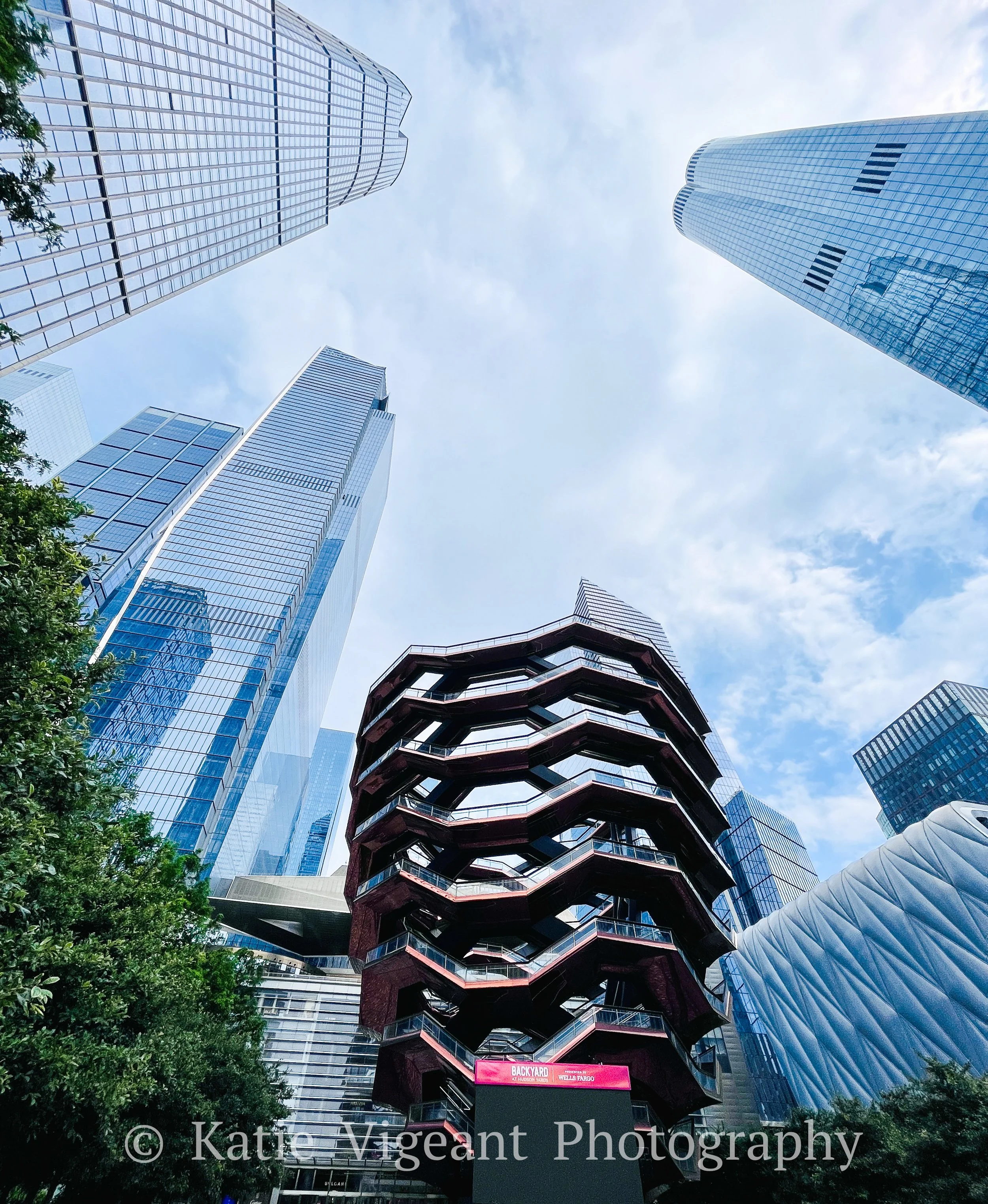 View of tall modern skyscrapers from the ground looking up in a cityscape, with a mix of glass and steel buildings and a cloudy sky.