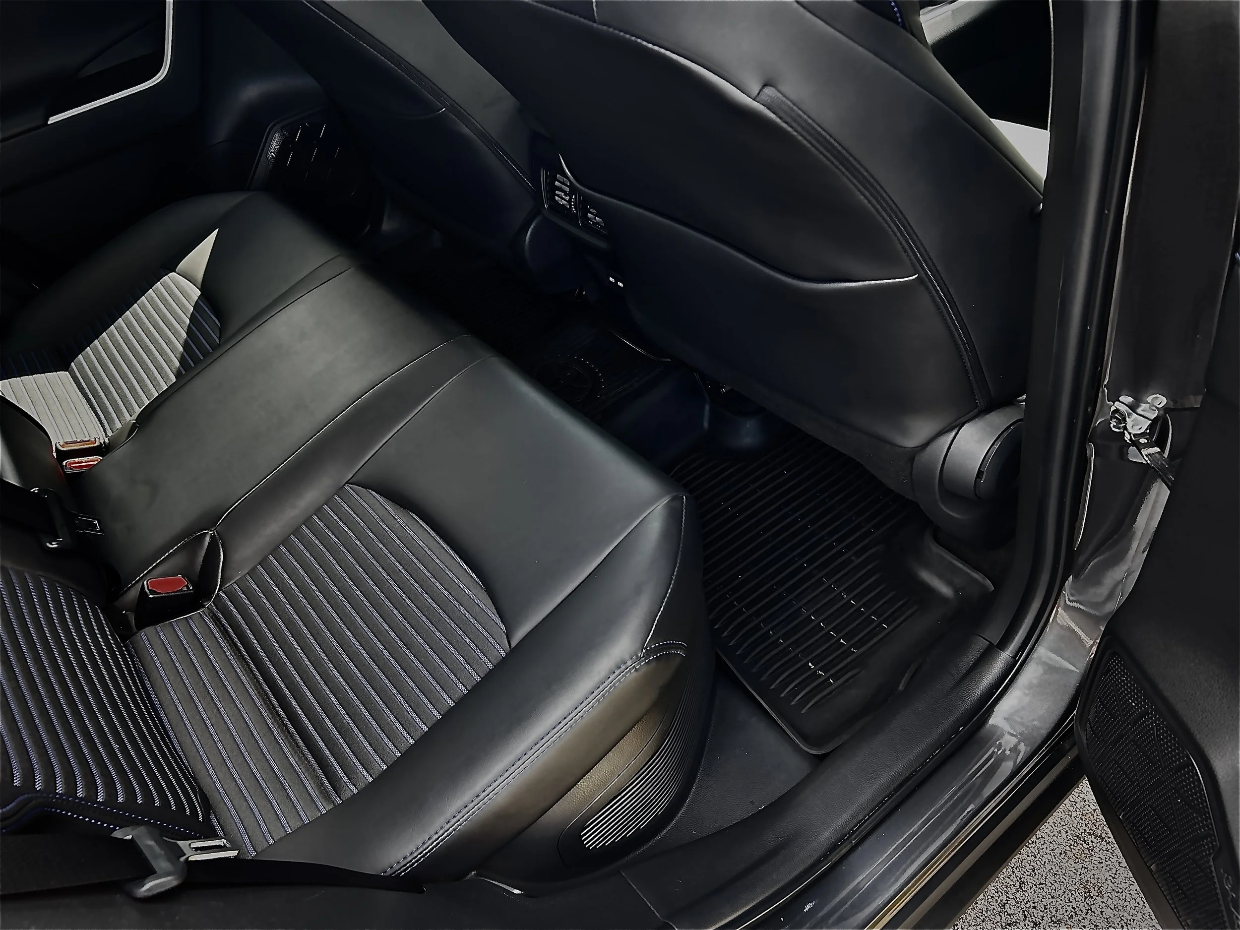 The interior of a vehicle showing the backseat area with black leather seats, a striped fabric pattern on the seat cushion, and rear air vents and controls on the back of the front seats.