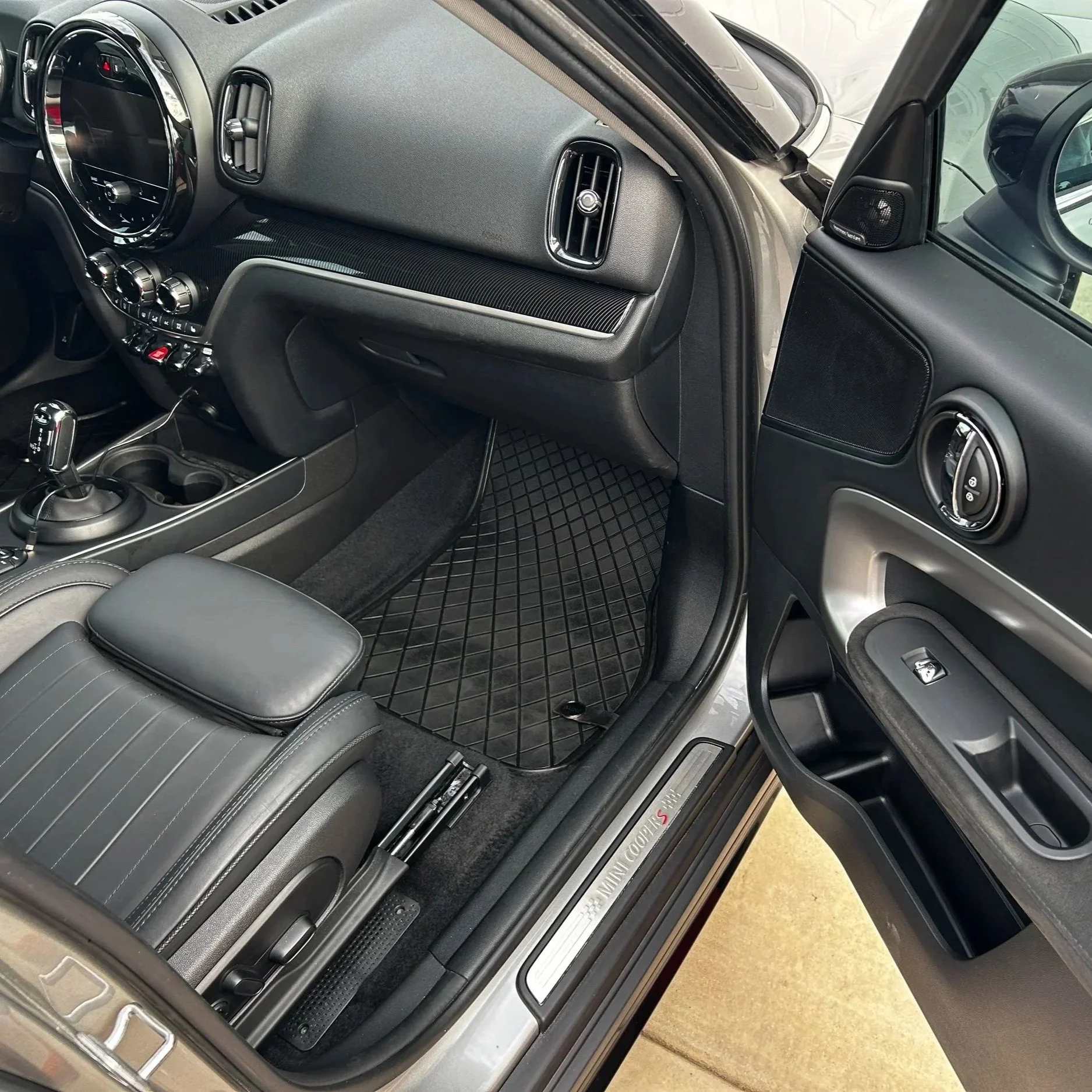 The interior of a luxury SUV showing the dashboard, center console with gear shifter, climate controls, and part of the leather seats. The vehicle appears to be a Mini Cooper S.