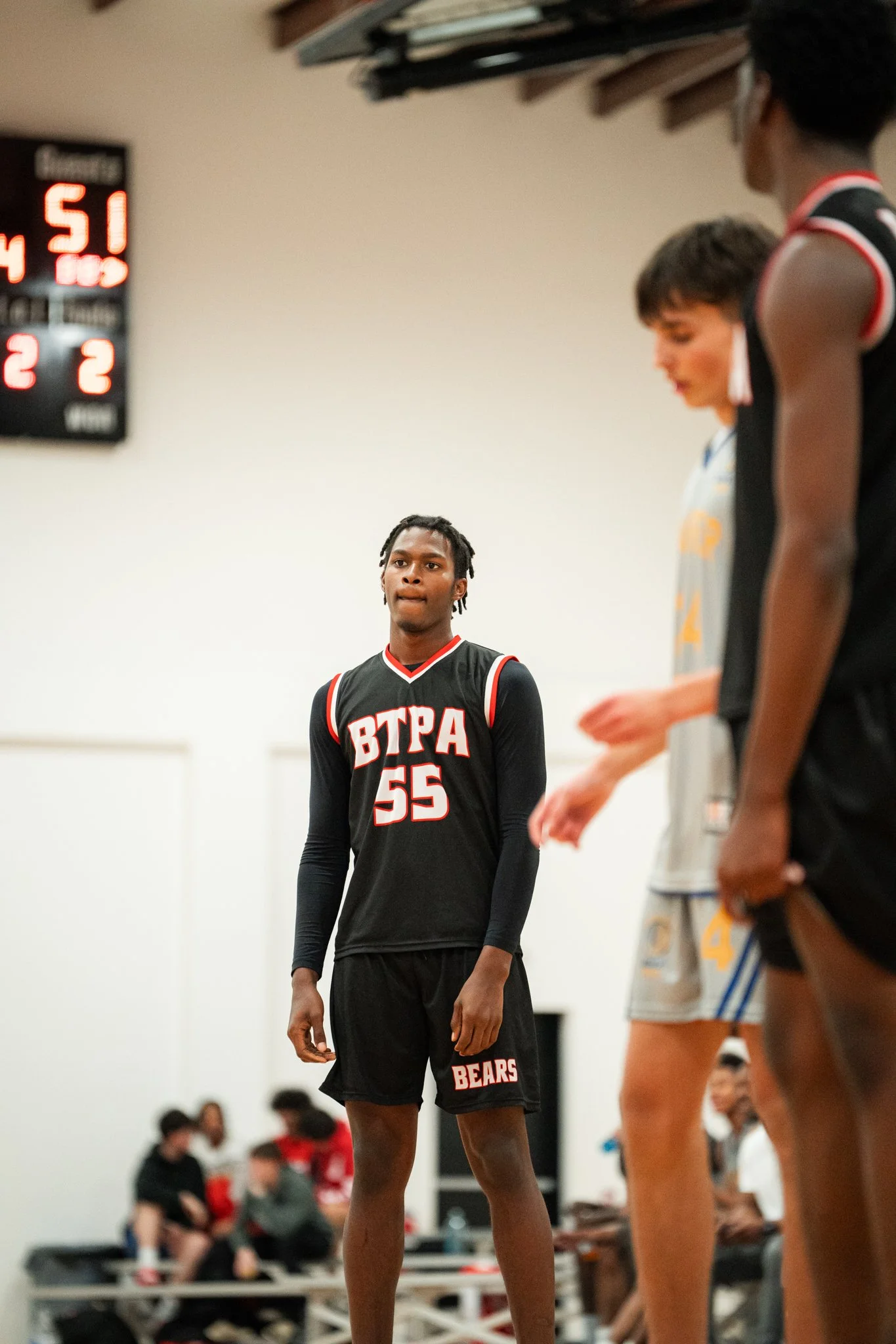 Basketball players on the court, with the main player wearing a black uniform with 'BTPA 55' and 'BEARS' written on it, standing in focus while others are blurred.