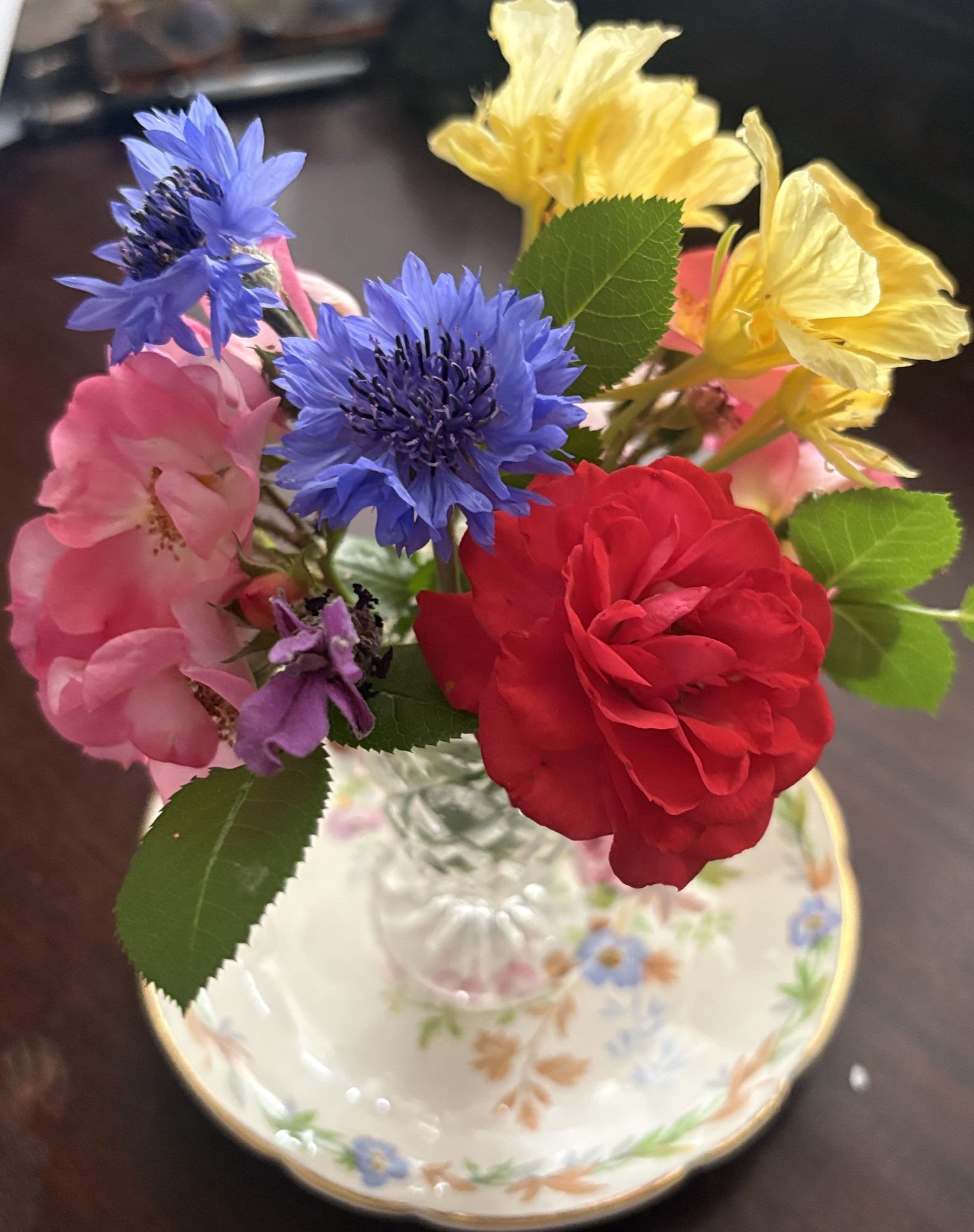 A posy of pink roses, red roses, blue cornflowers and yellow nasturtiums in a crystal vase