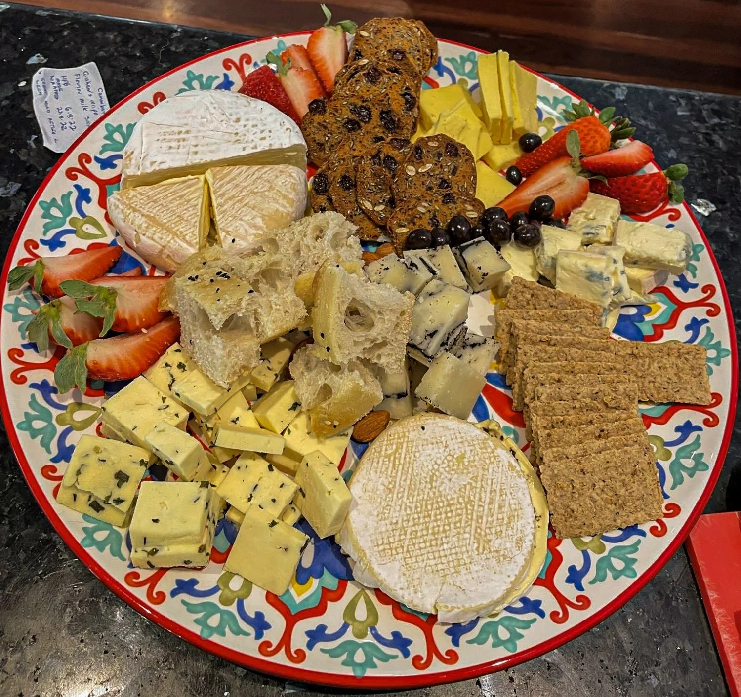 Homemade cheese board with brie, blue cheese and herb cheeses, served with strawberries, grapes, crackers and rustic bread on a decorative plate.