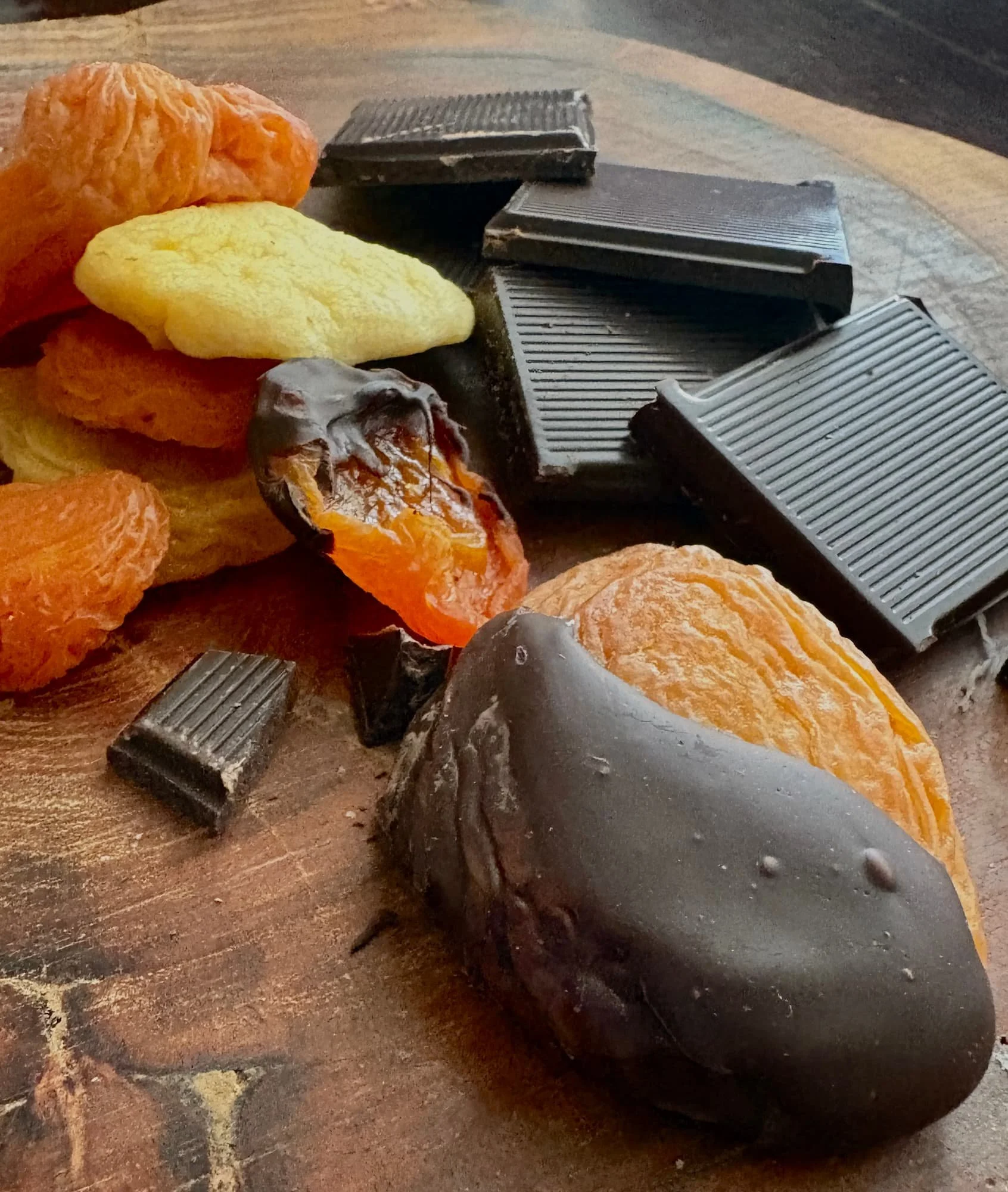 dried fruit, squares of dark chocolate and a chocolate dipped dried peach on a wooden board