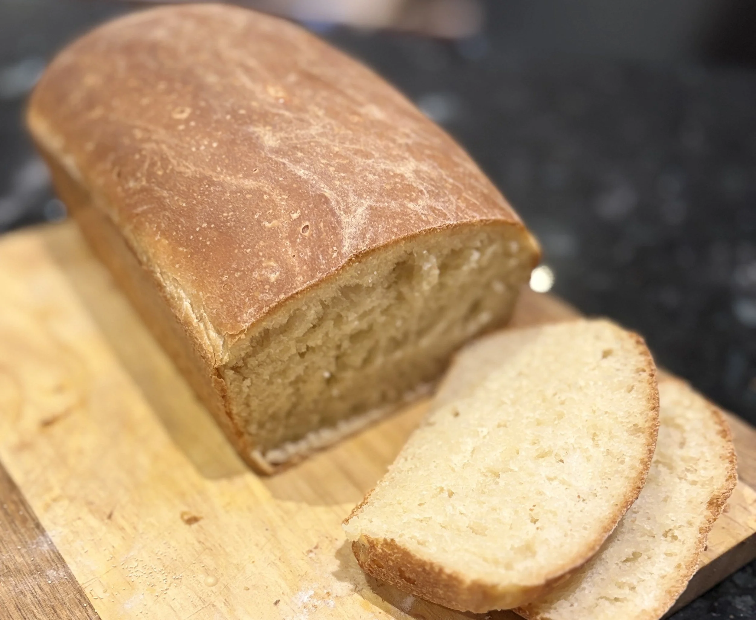 Freshly baked homemade bread loaf sliced on a wooden board, revealing a light, fluffy interior and crisp golden crust.