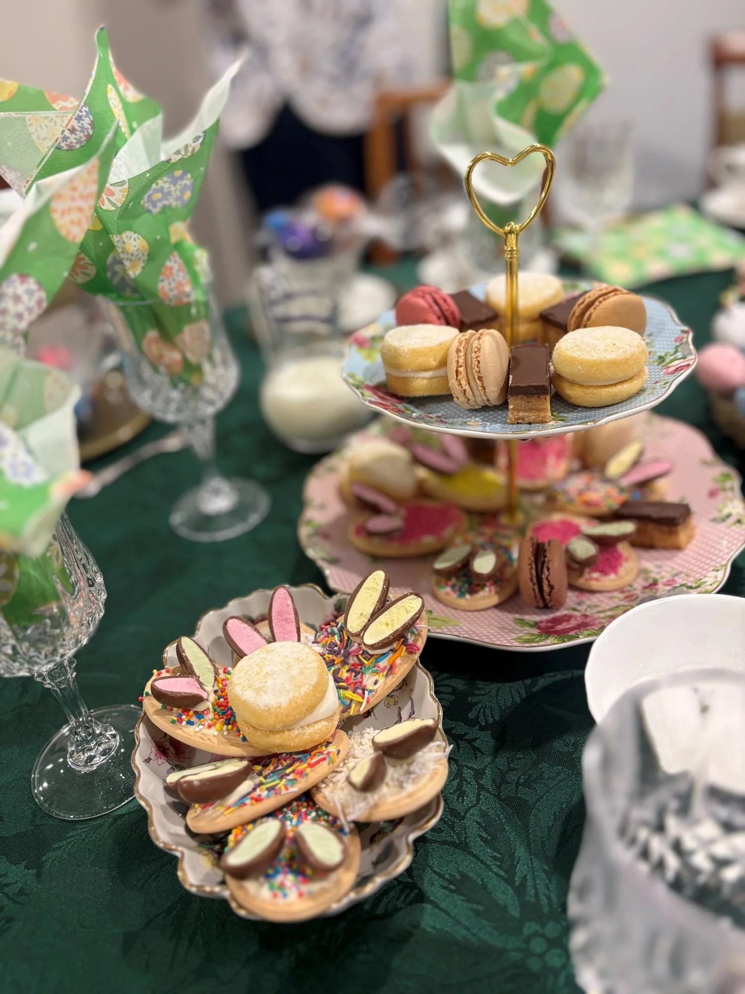 Small dish with decorated biscuits in the foreground and tiered cake stand filled with sweet treats in the back ground