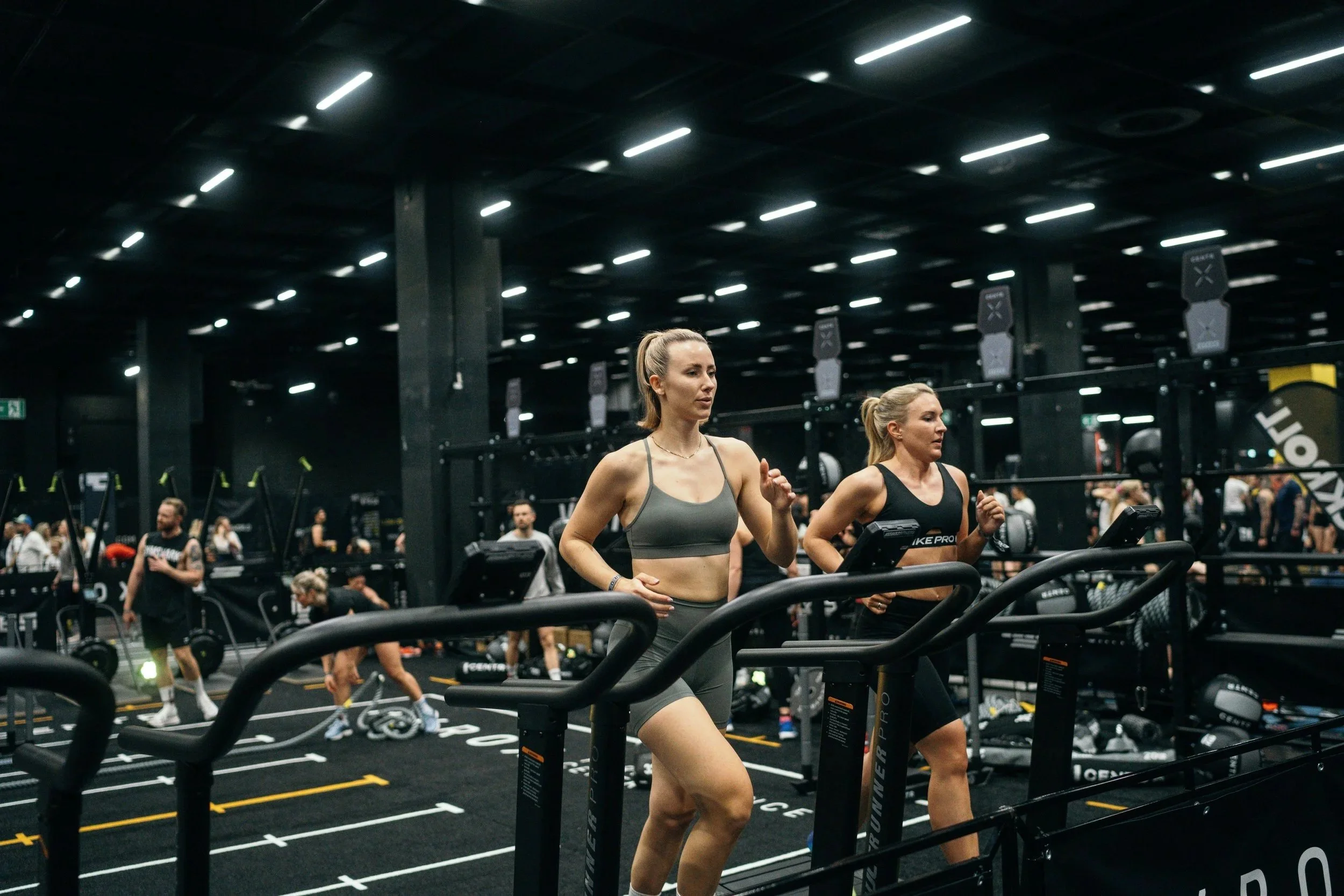 HYROX event image. Two women using official HYROX equipment to warm up for a HYROX event.