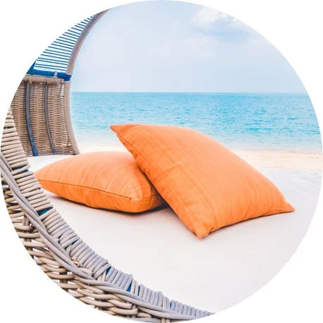 Two orange pillows on a white lounge chair on the beach with ocean and sky in the background.