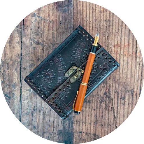 A vintage black metal rectangular box with decorative engravings, a fountain pen with an orange body and gold accents, and a small brass key, all on a wooden surface.