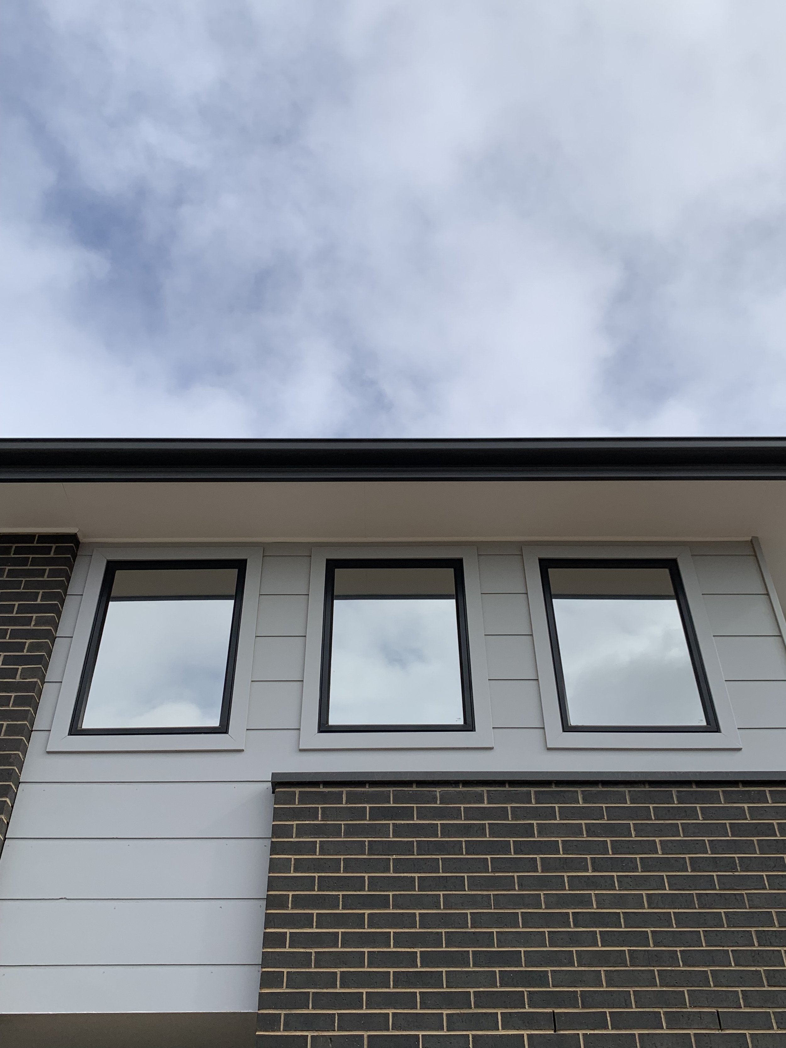 Close-up of the upper part of a modern house with three rectangular windows tinted. 
