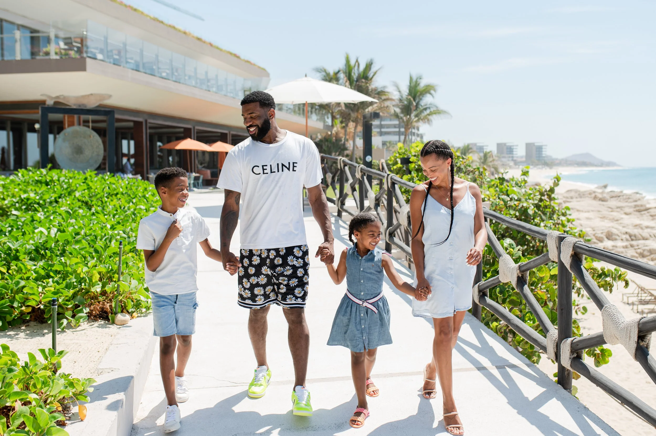 Una familia paseando por un paseo junto a la playa en un día soleado, sonriendo y disfrutando el momento.