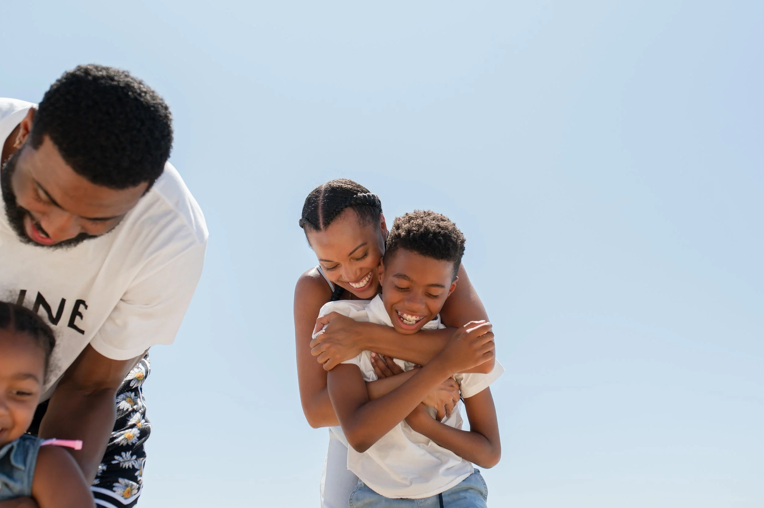 Familia feliz abrazándose y riendo al aire libre con cielo azul.