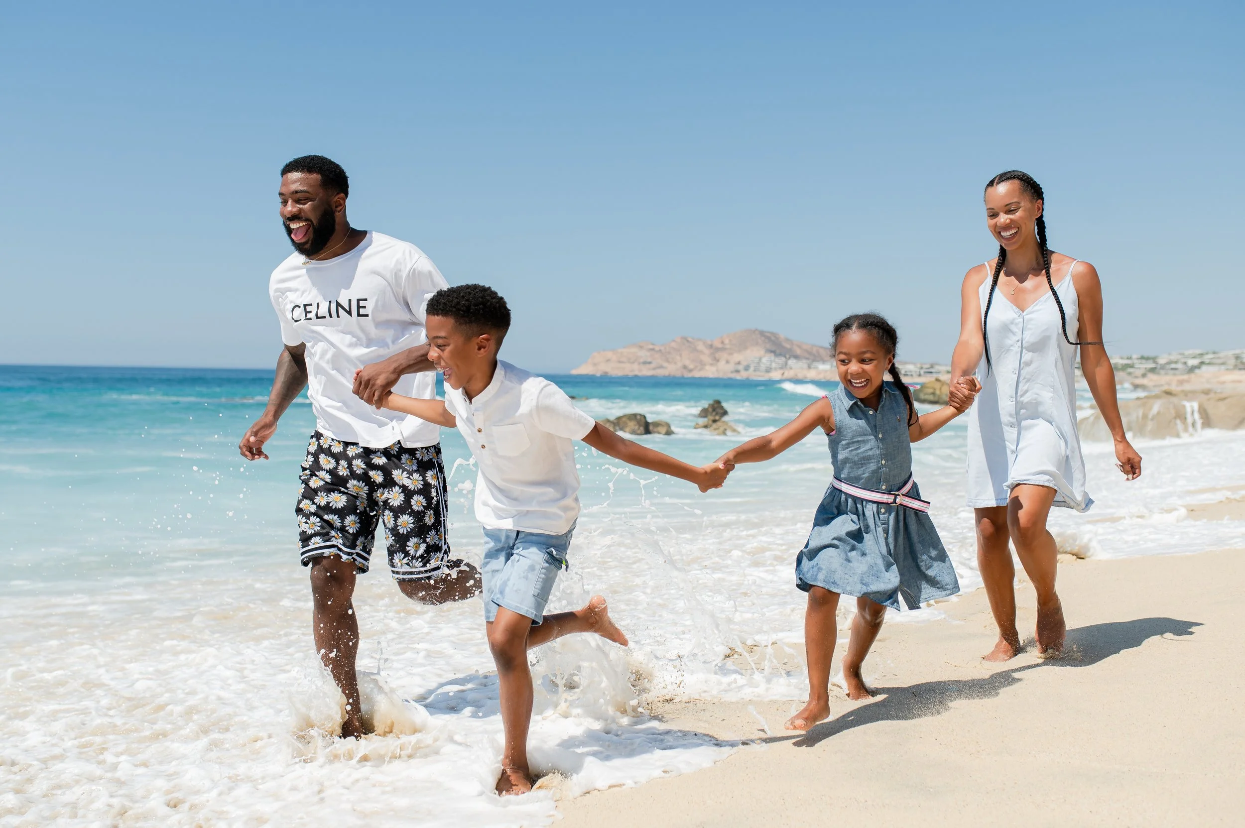 Familia disfrutando en la playa, corriendo y jugando en la arena cerca del agua, con un fondo de mar y cielo azul.