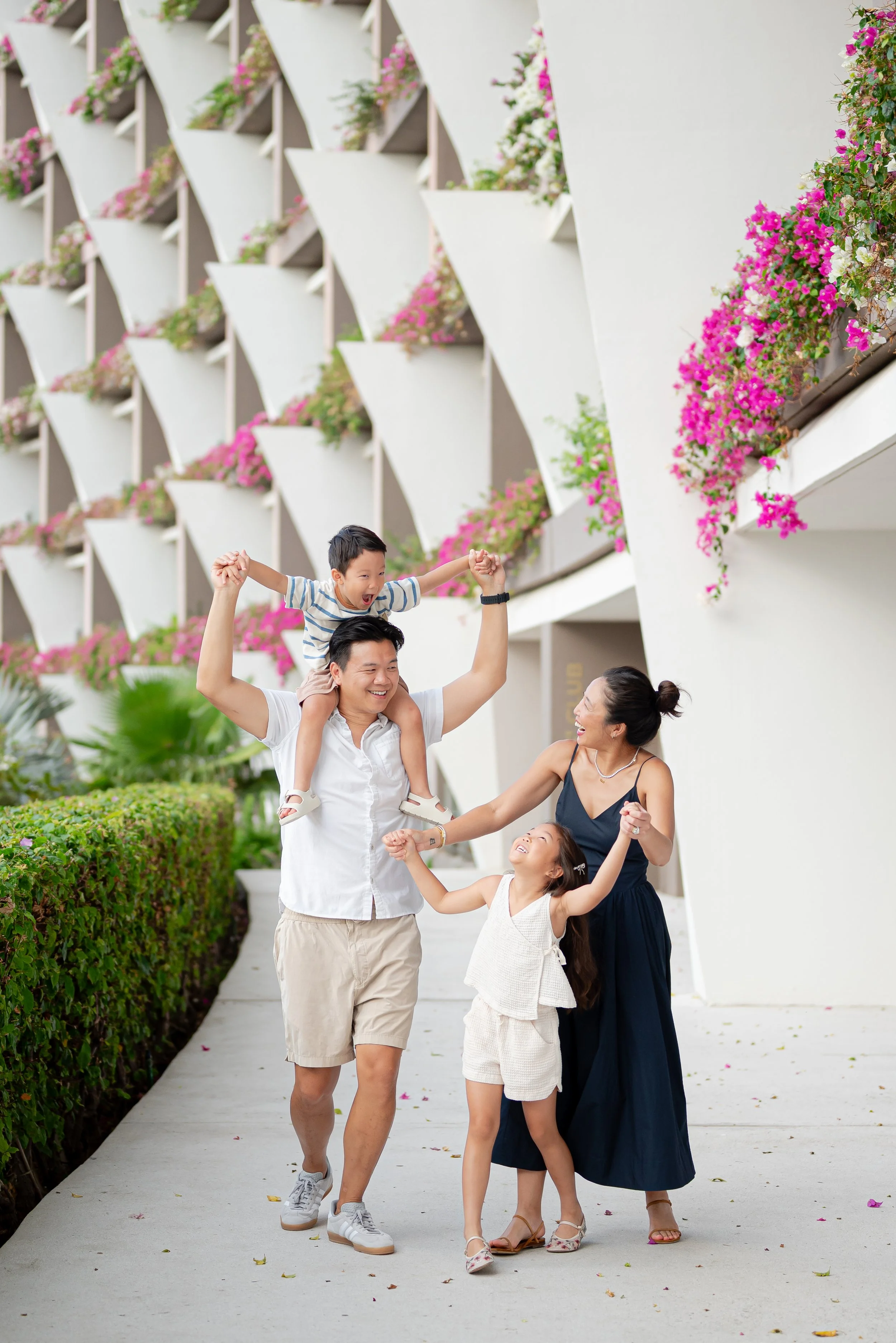 Familia feliz paseando al aire libre frente a un edificio moderno con paredes decoradas con flores rosas y blancas.
