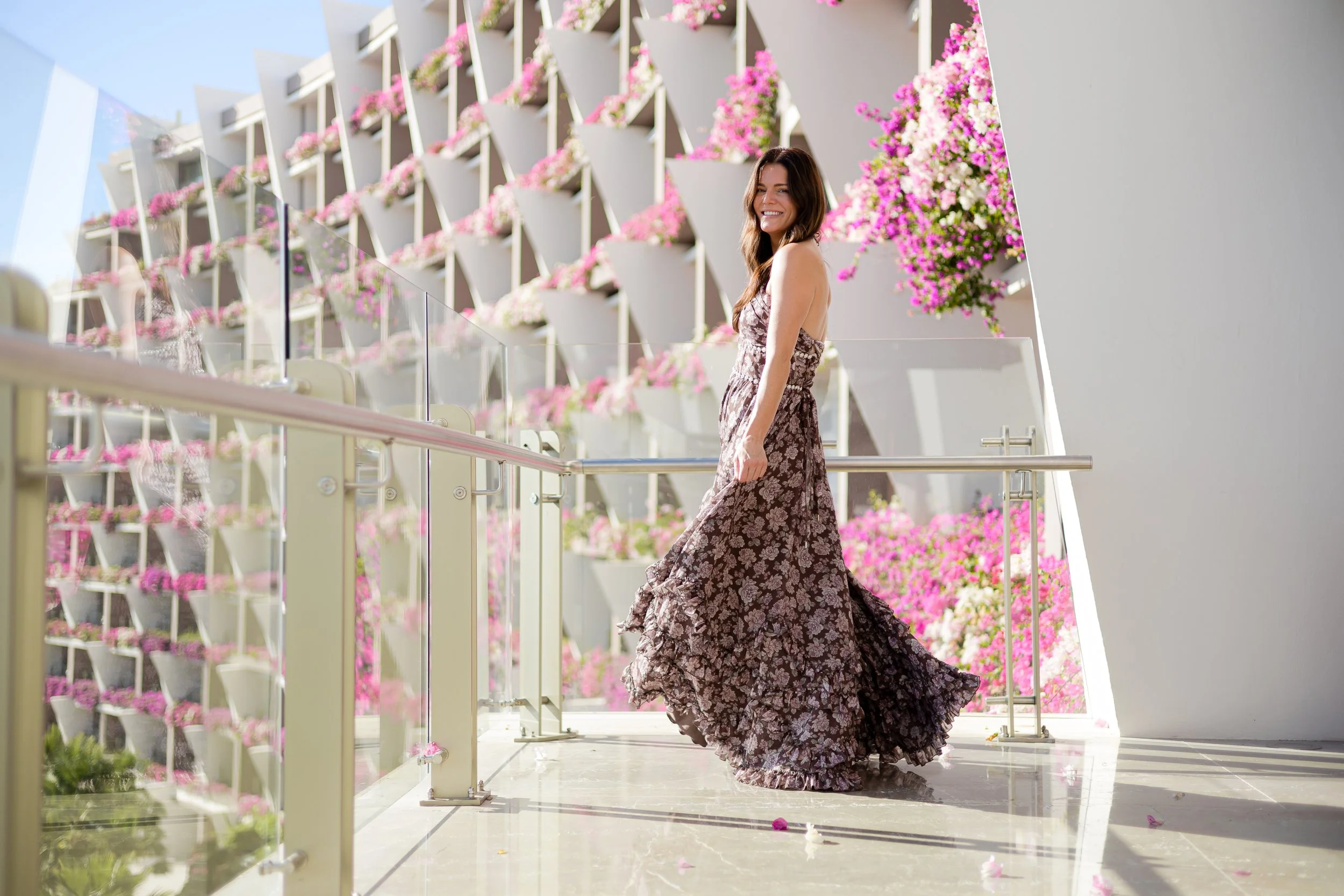 Mujer sonriendo en un balcón decorado con flores rosas y blancas.