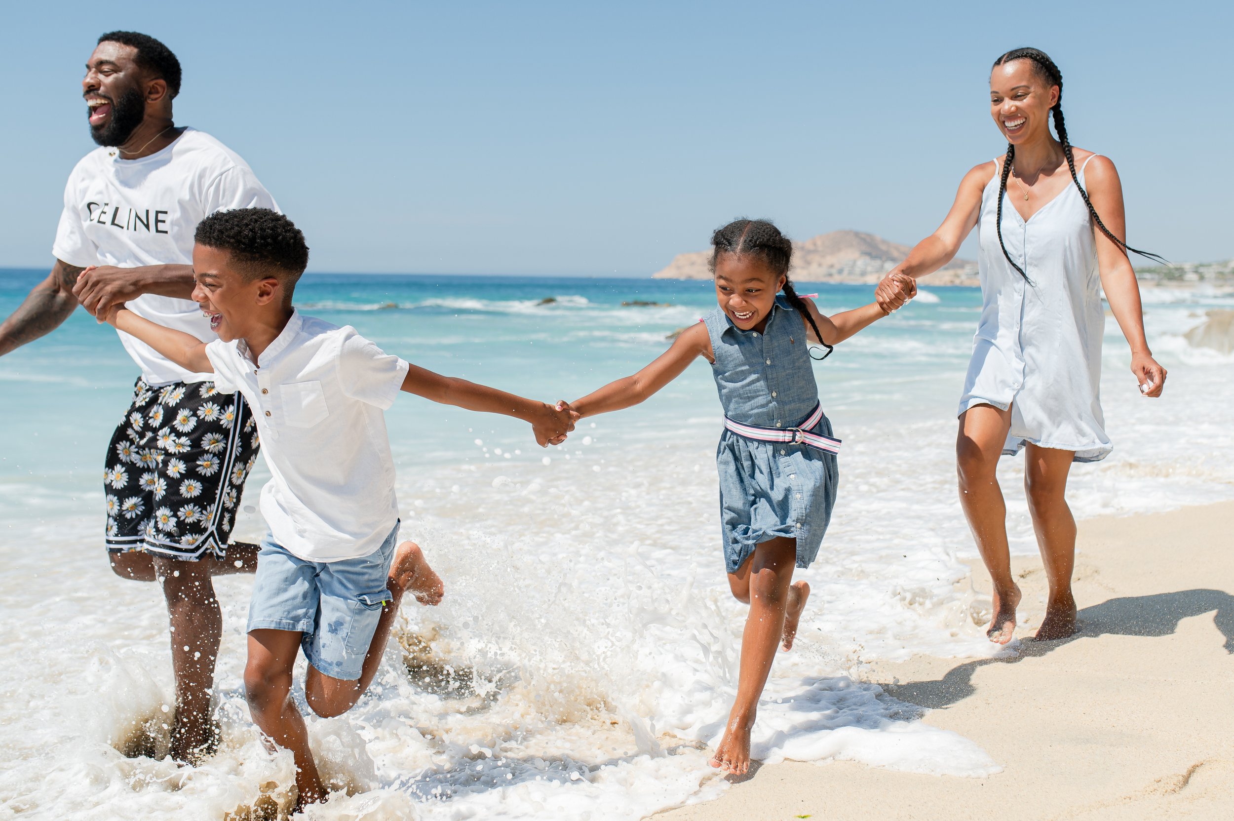 Familia feliz disfrutando en la playa, corriendo por la arena y el agua, con fondo de mar y cielo despejado.