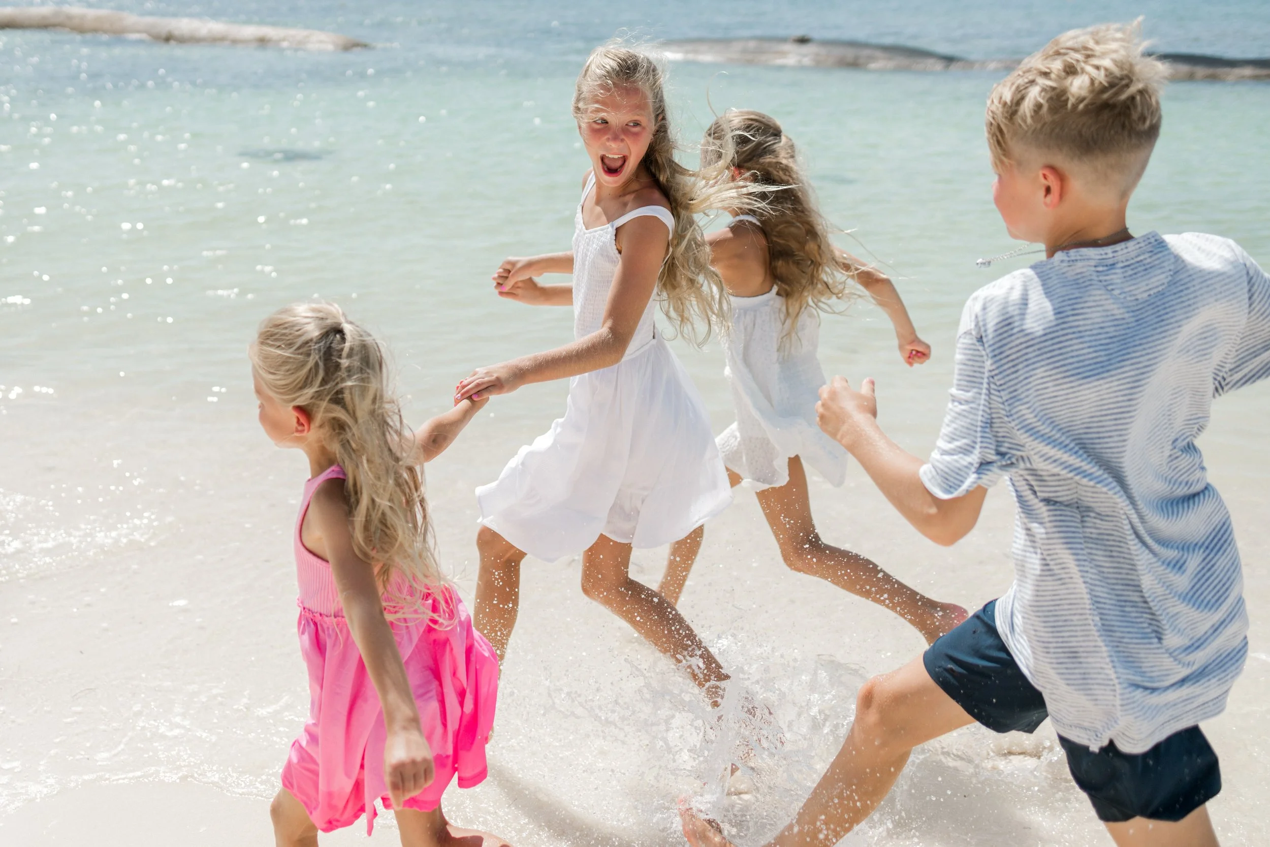 Niños jugando en la playa con agua y arena, todos felices.