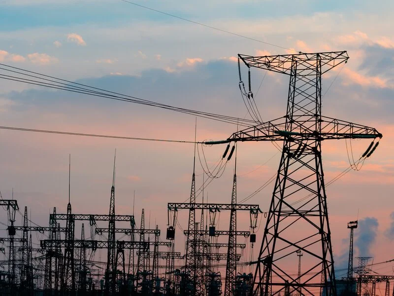 Una serie de torres de alta tensión y cables que transportan electricidad contra un cielo al atardecer.