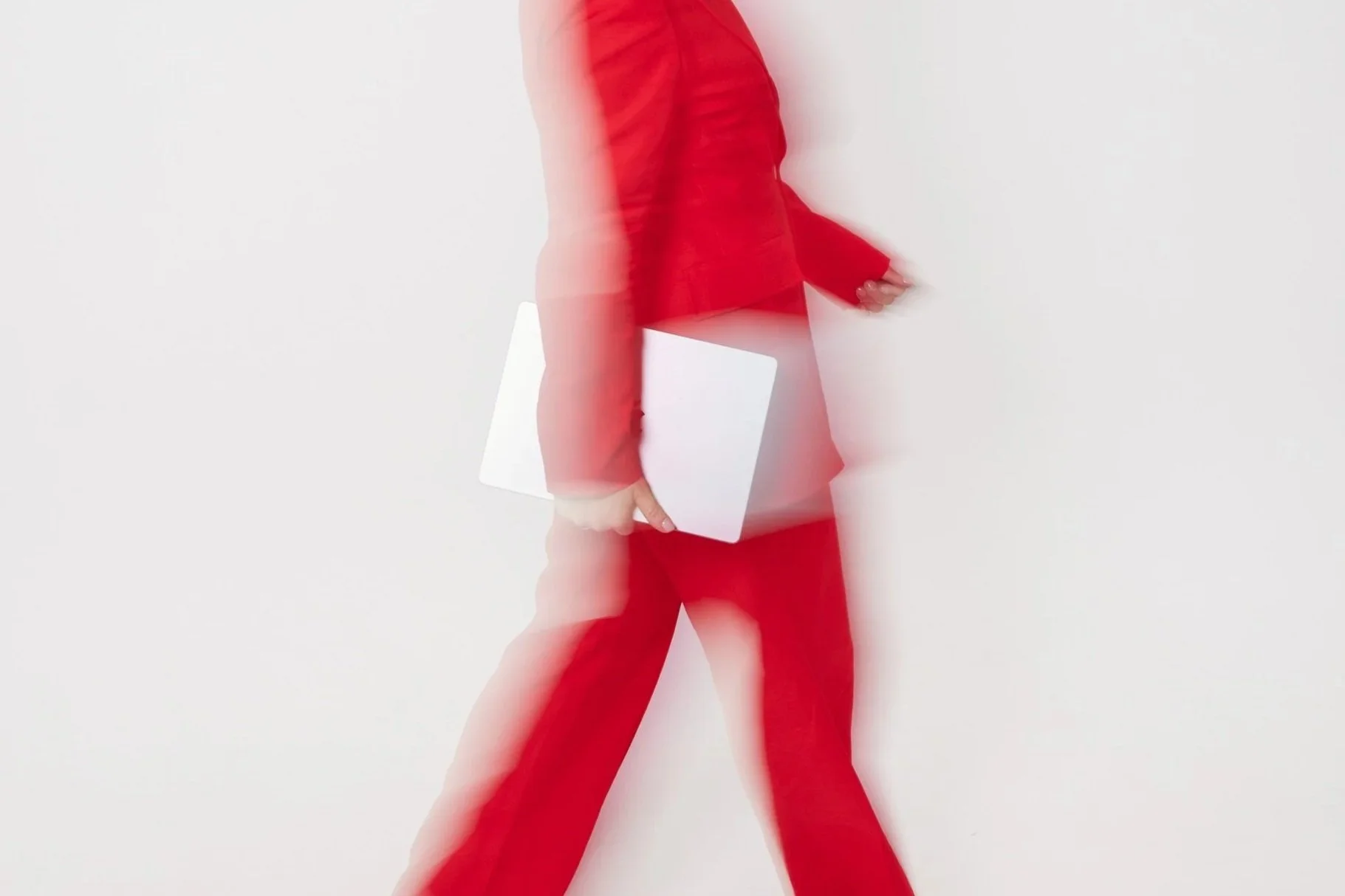 Person dressed in red pants and a red blazer walking with two white notebooks, with motion blur effects.