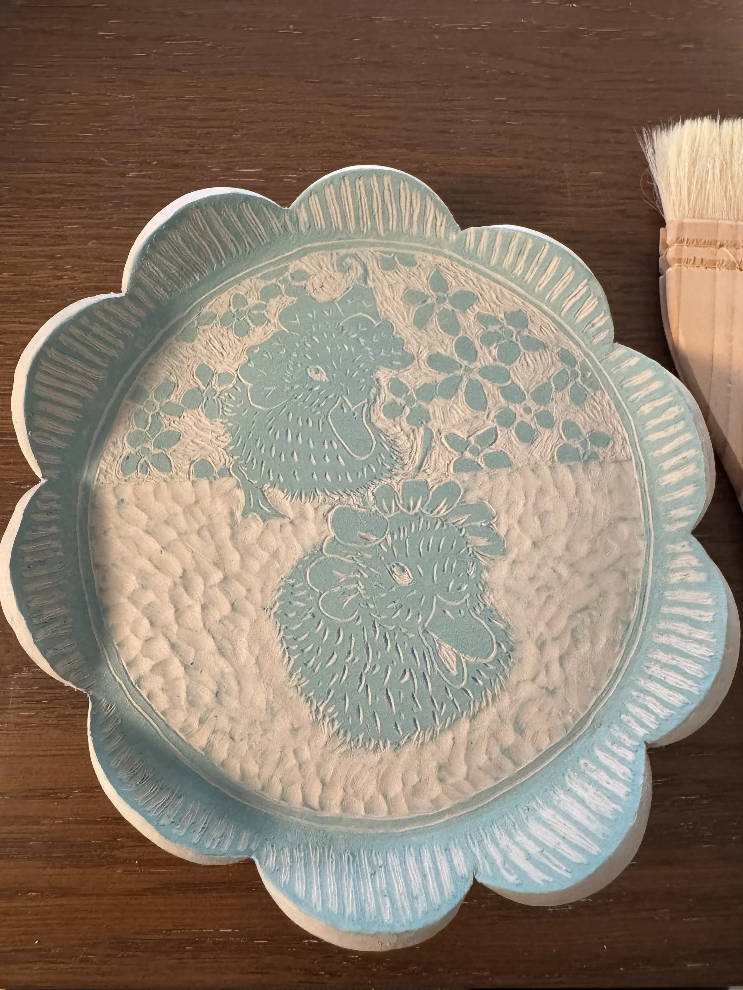 A ceramic scalloped plate with two ducklings wearing flower hats - illustrated in sgraffito