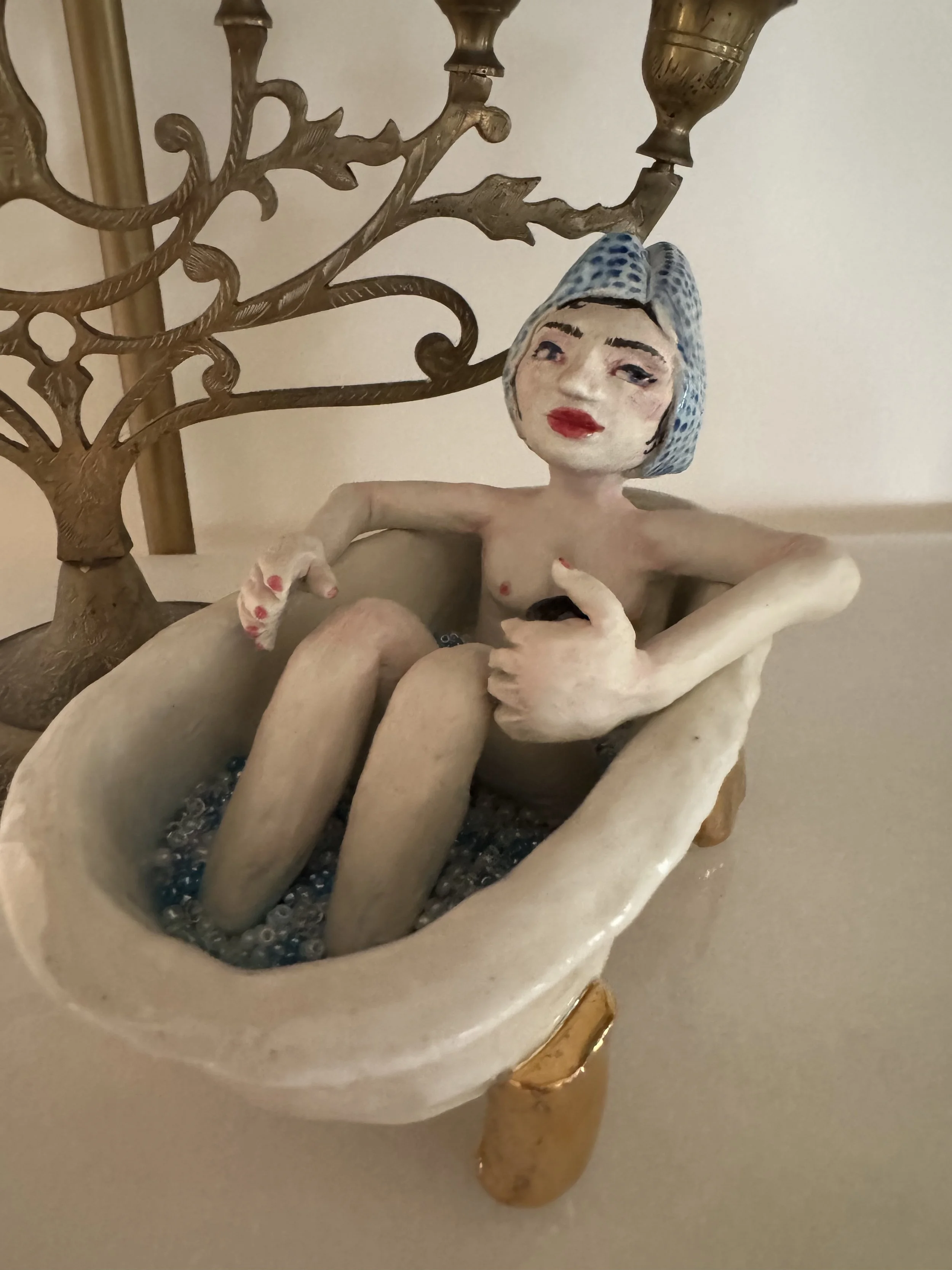 "Sophia in the bath" A ceramic figurine of a woman with a blue towel in her hair and red lips. She has a matcha in her hand.