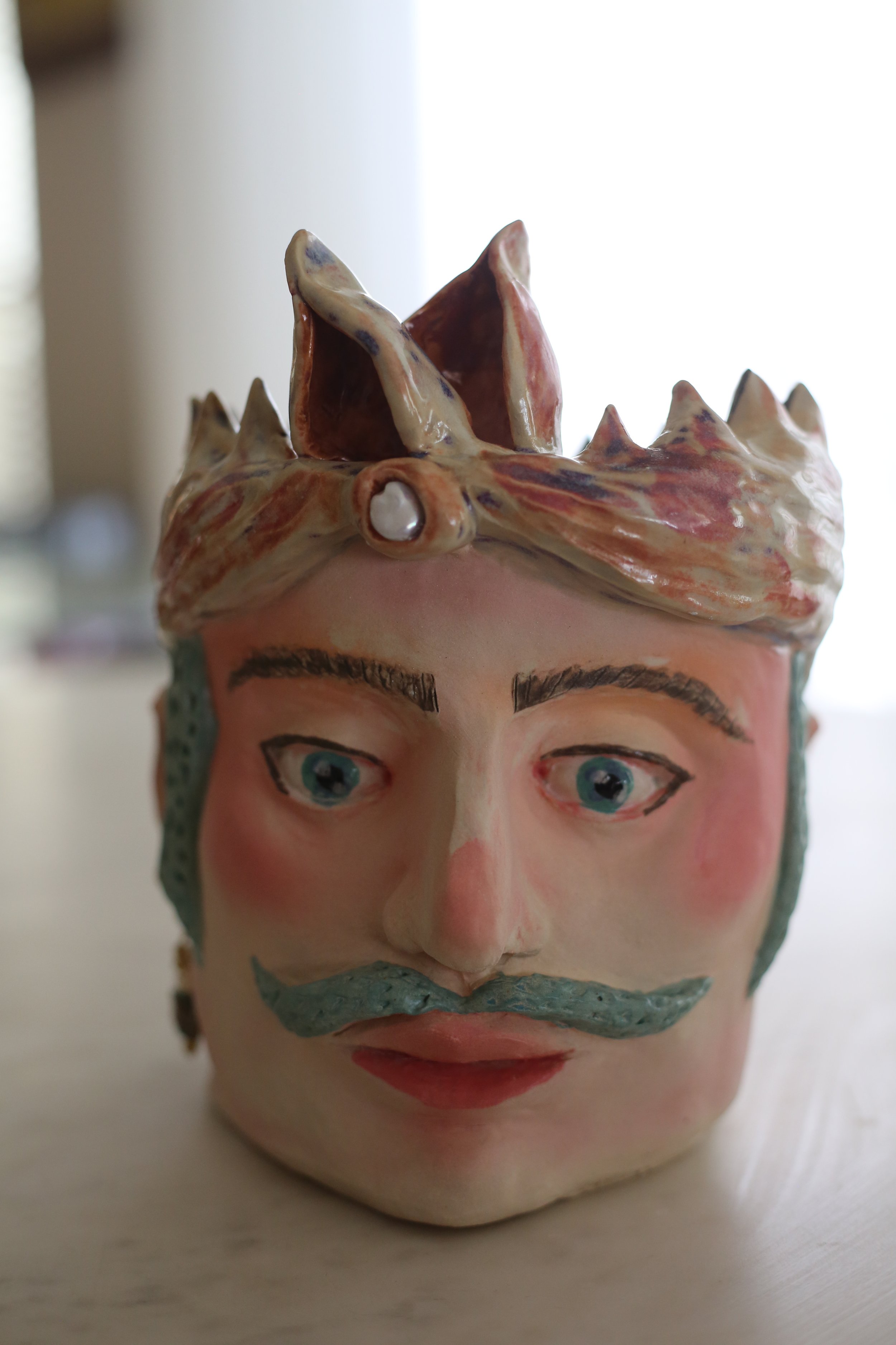 "Guillermo" Ceramic Sicilian Head by Amy Ambrose. Front view. Blue eyes, eyebrows and moustache, with a crown-like top featuring a real pearl and pearl earring. 