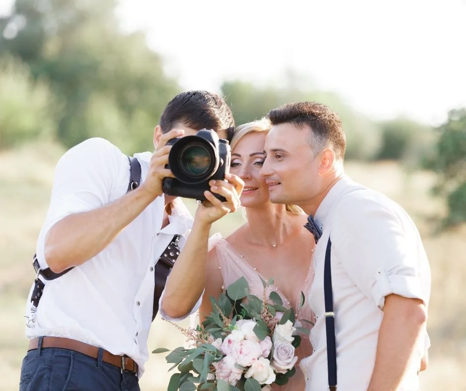 A photographer takes a picture of a bride and groom in an outdoor setting.