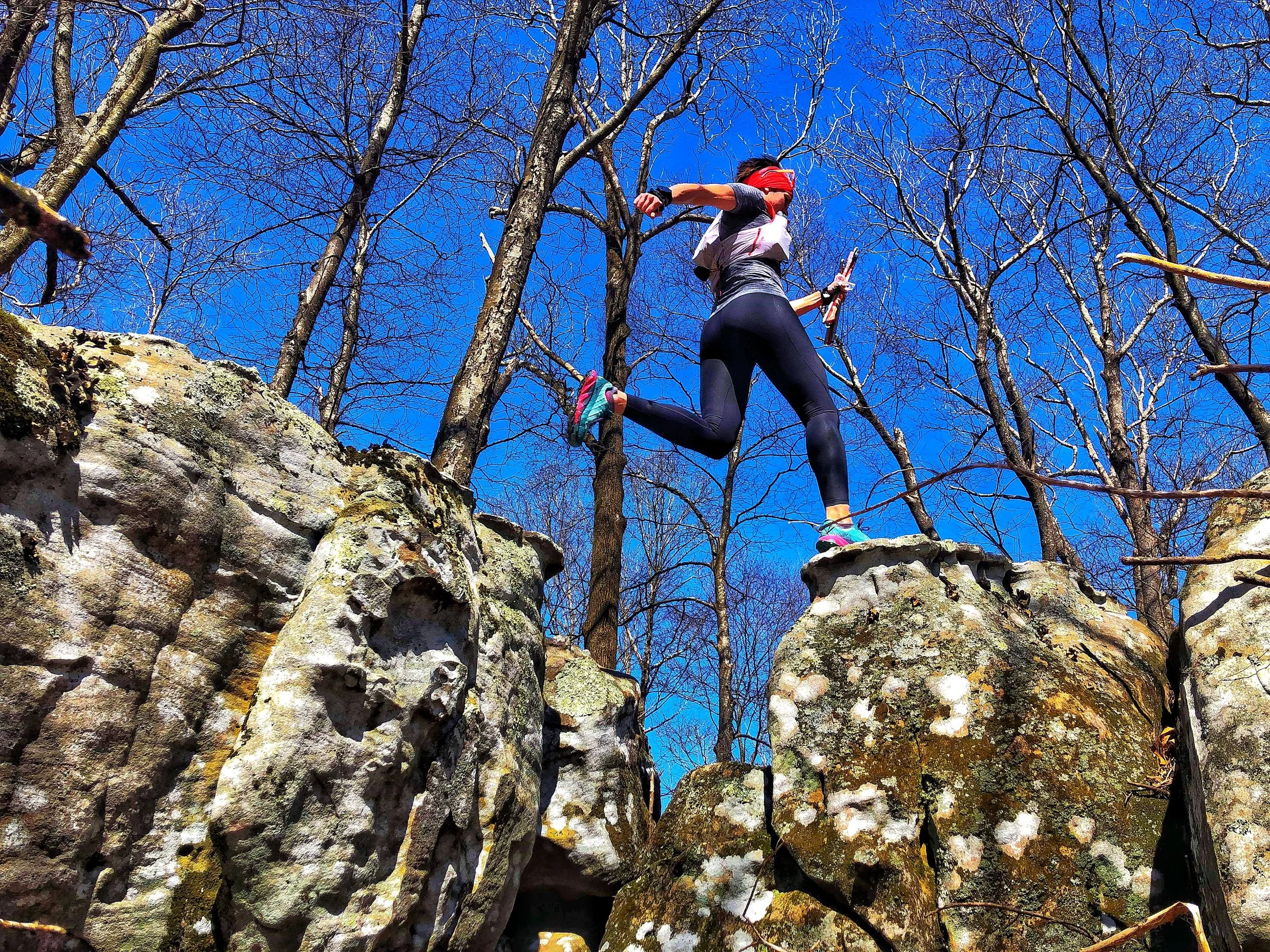 Stephanie Case trail running on rocky terrain surrounded by leafless trees with a bright blue sky in the background in Tennessee just days before the start of the Barkley Marathons.