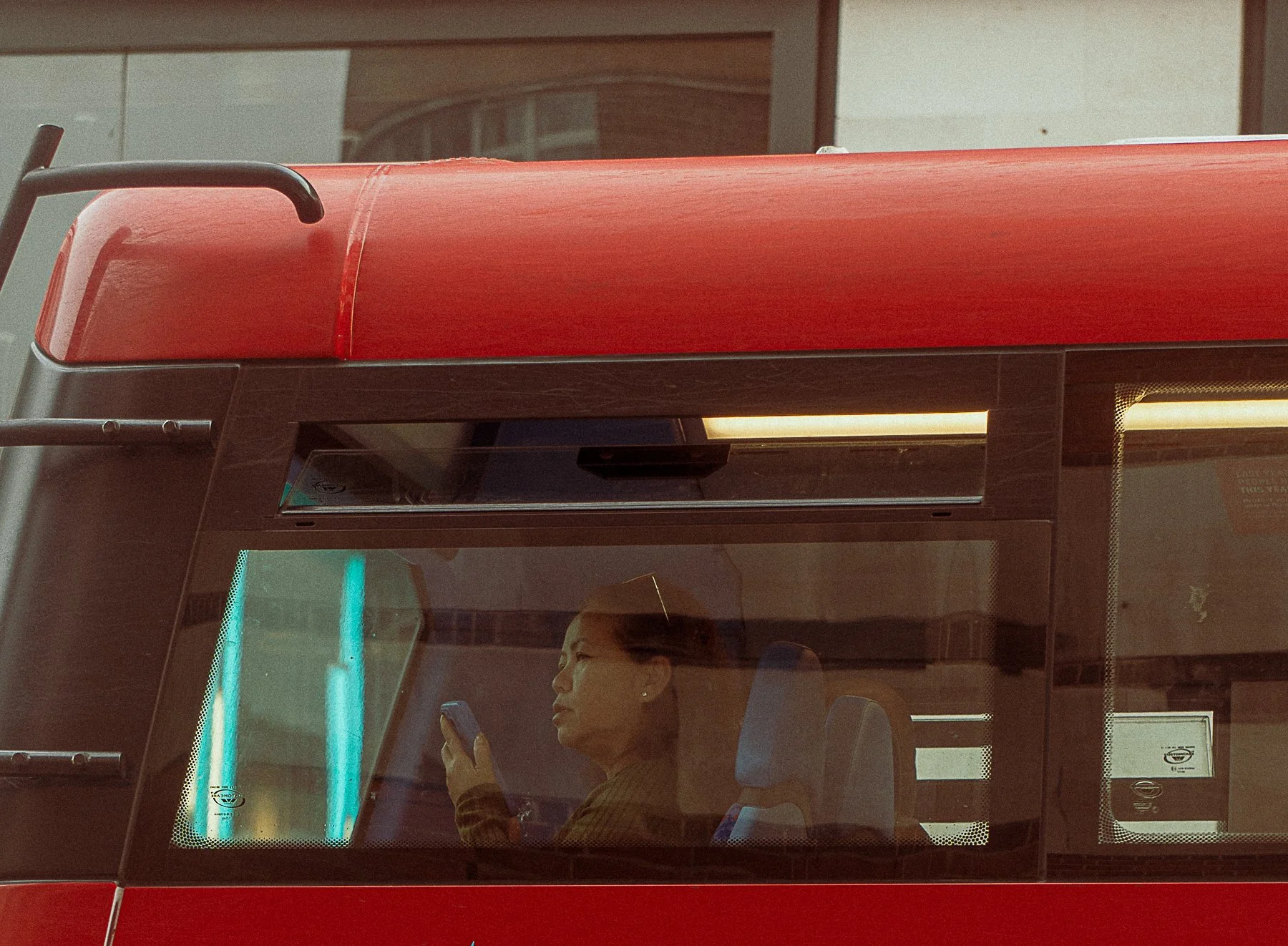Woman sitting inside a red bus looking at her phone.