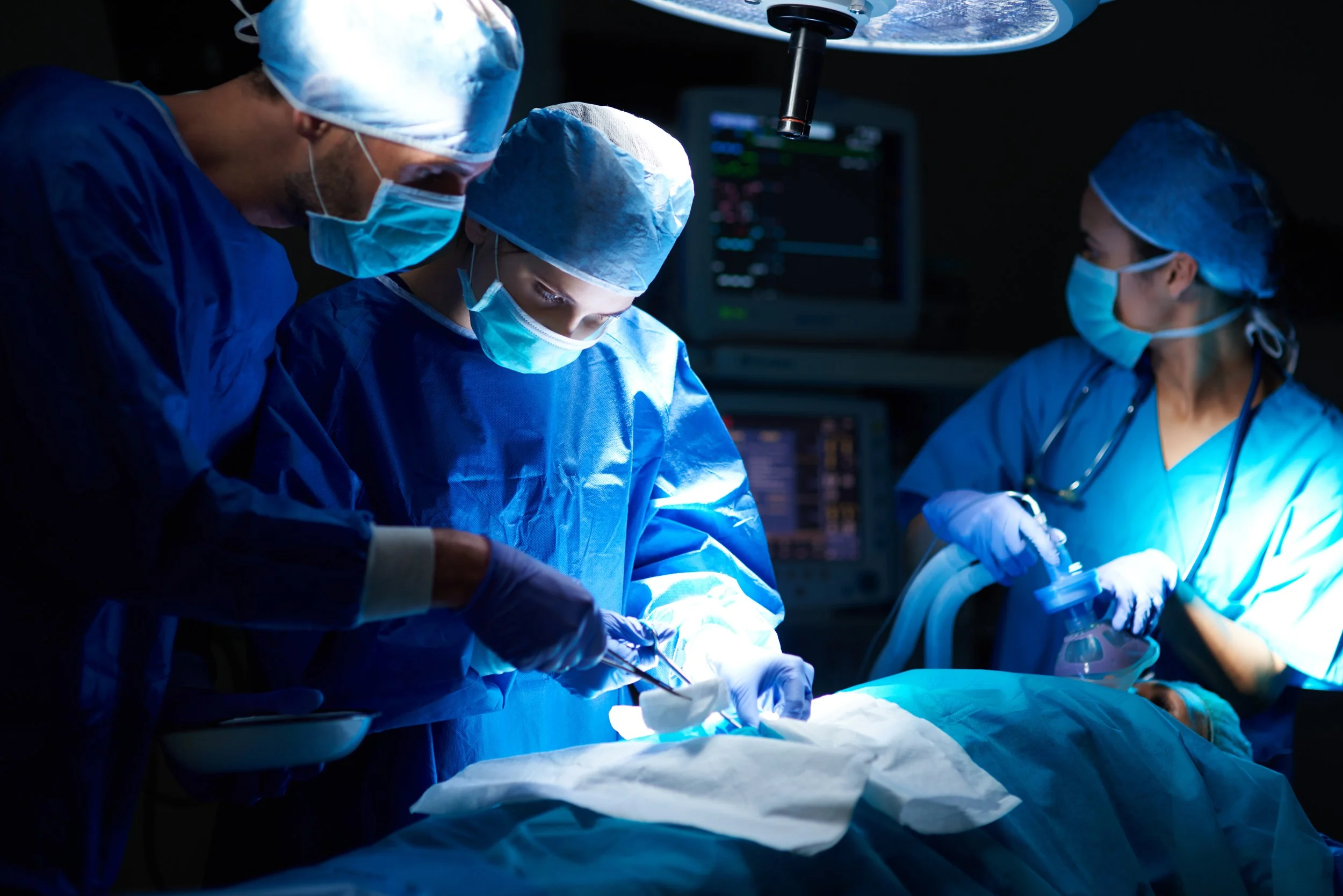 Medical team performing surgery in an operating room, wearing surgical masks, gowns, and gloves.