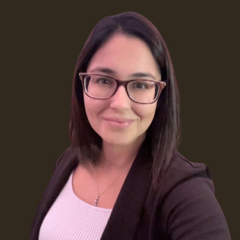 Headshot of Lyndsay Sylvester, a woman with shoulder-length dark hair and glasses, wearing a white top and a black blazer, smiling at the camera.