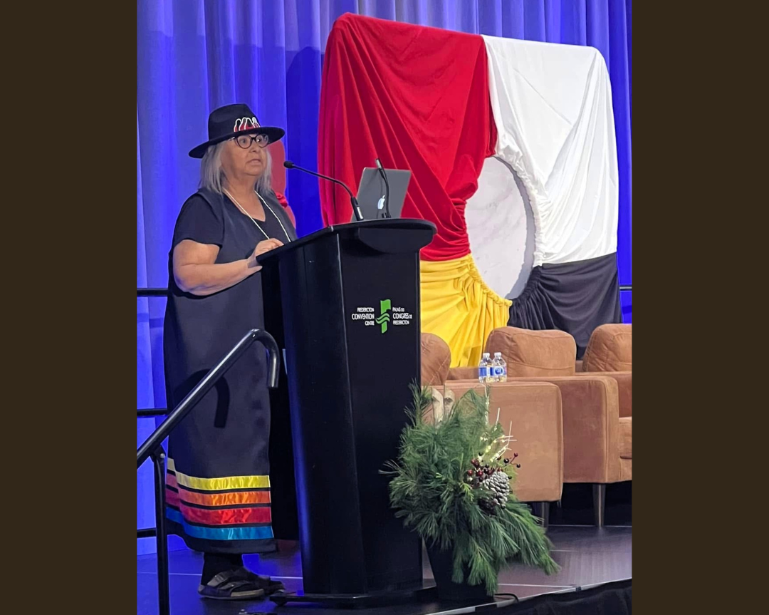 Conference presentation focused on Indigenous research and knowledge sharing, with a speaker addressing the audience from a podium.